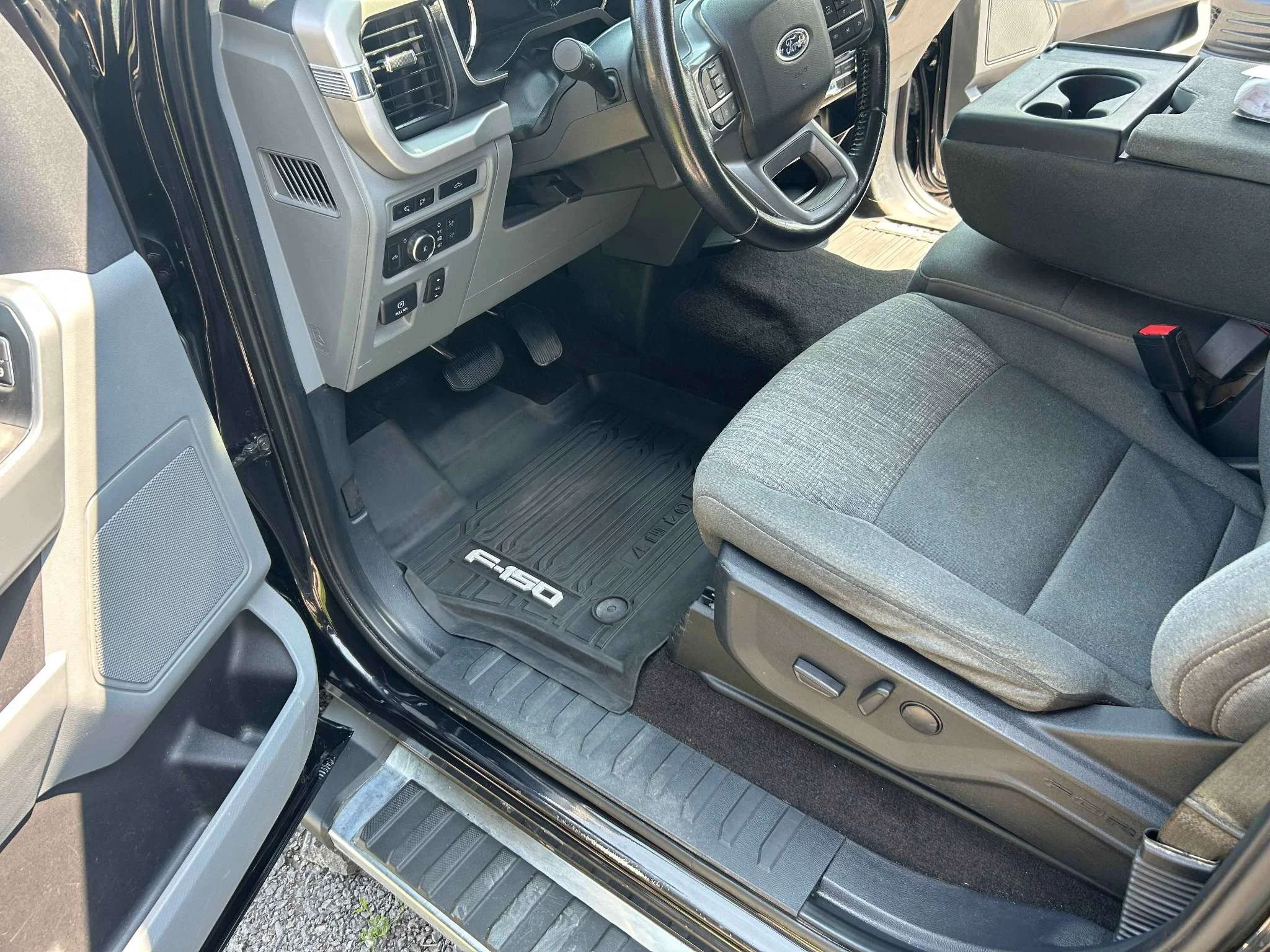 Interior view of a Ford F-150 truck showing the driver's seat, steering wheel, and dashboard with control buttons, and the floor mat with the F-150 logo.
