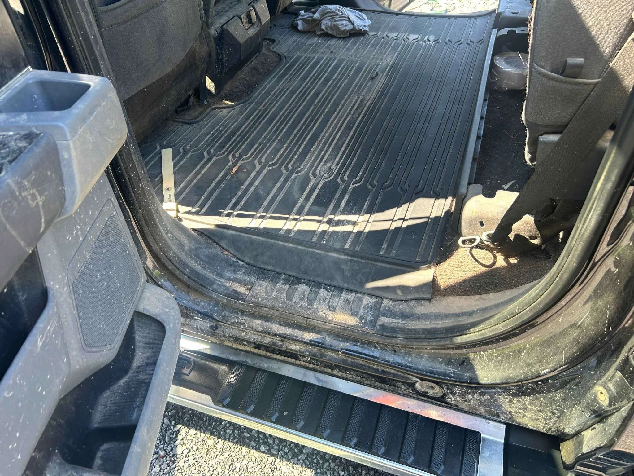 The interior of a vehicle showing a black rubber floor mat, with a pair of scissors and some dust and debris on the floor.