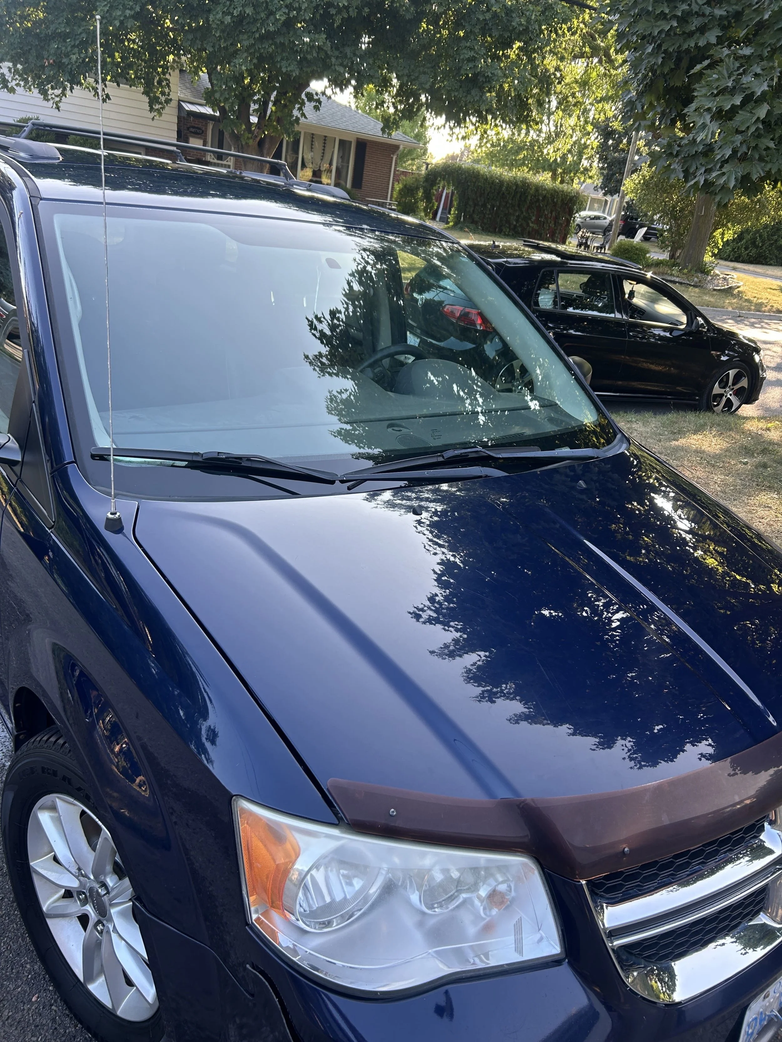 A blue SUV and a black sedan parked on a residential street with trees and houses in the background.