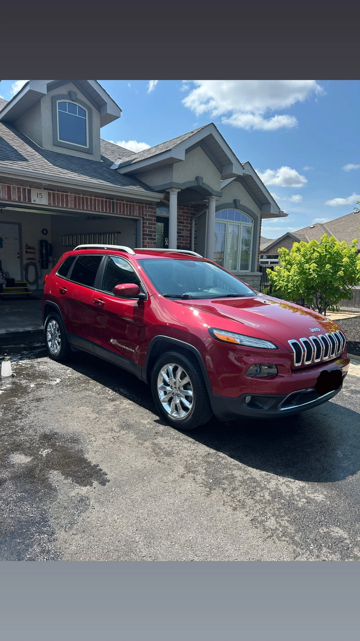Red Jeep SUV parked in front of a house with a brick and gray exterior on a sunny day.