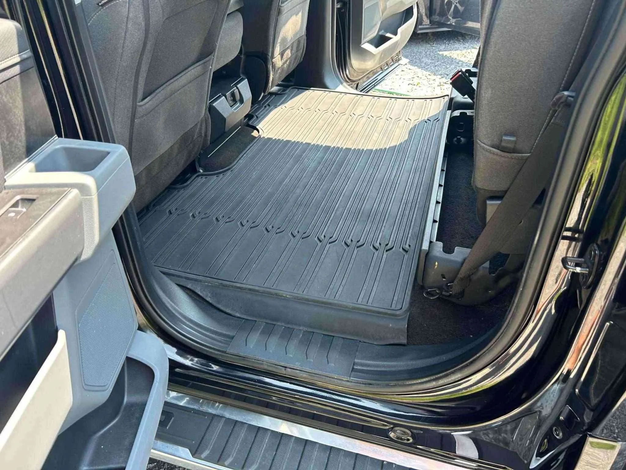 The interior of a vehicle showing the back seat area with a large rubber cargo mat on the floor and a gray storage container attached to the side of the open door.