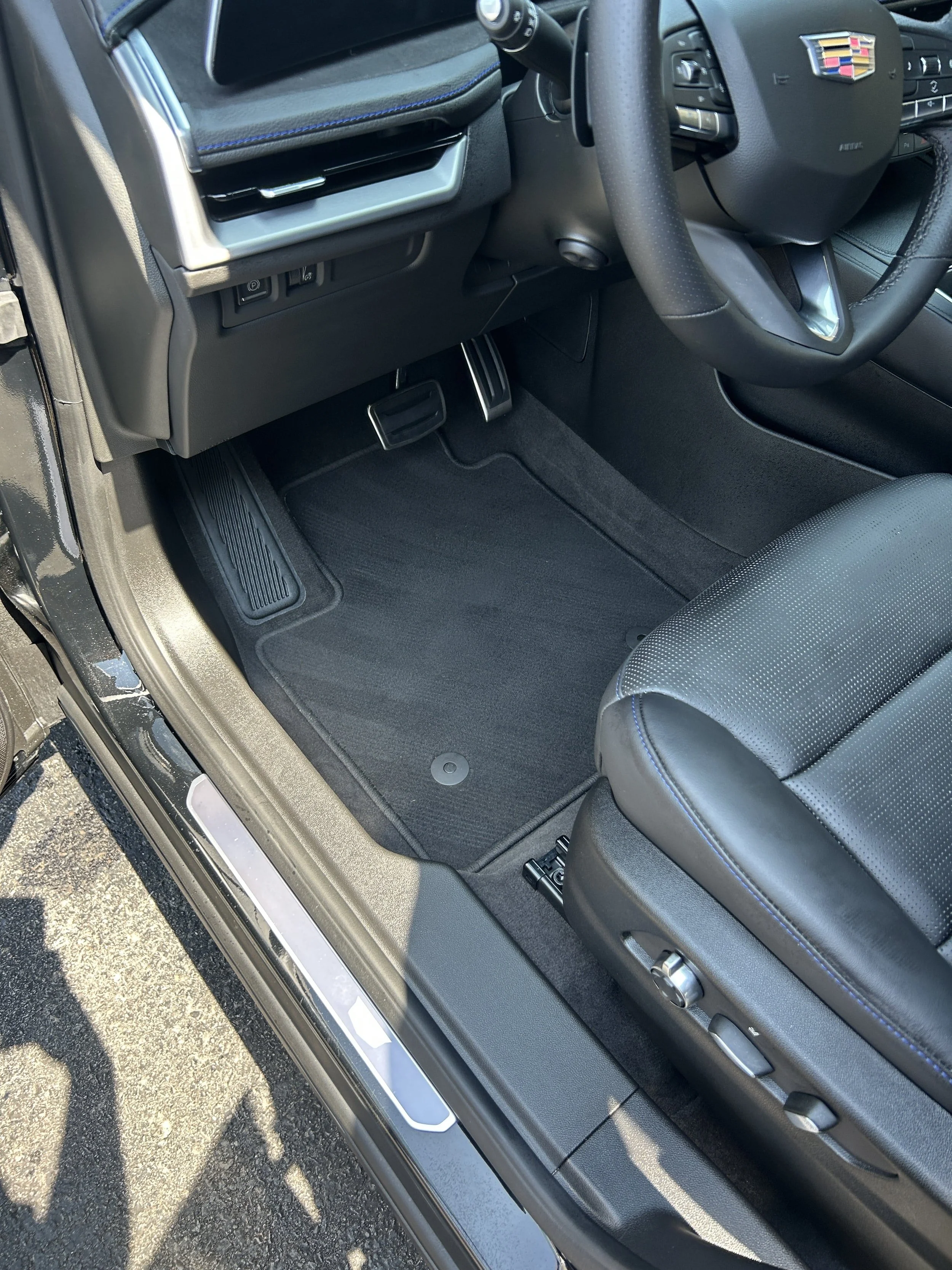 Interior of a Cadillac vehicle showing the driver's seat, steering wheel, pedals, and floor mat.