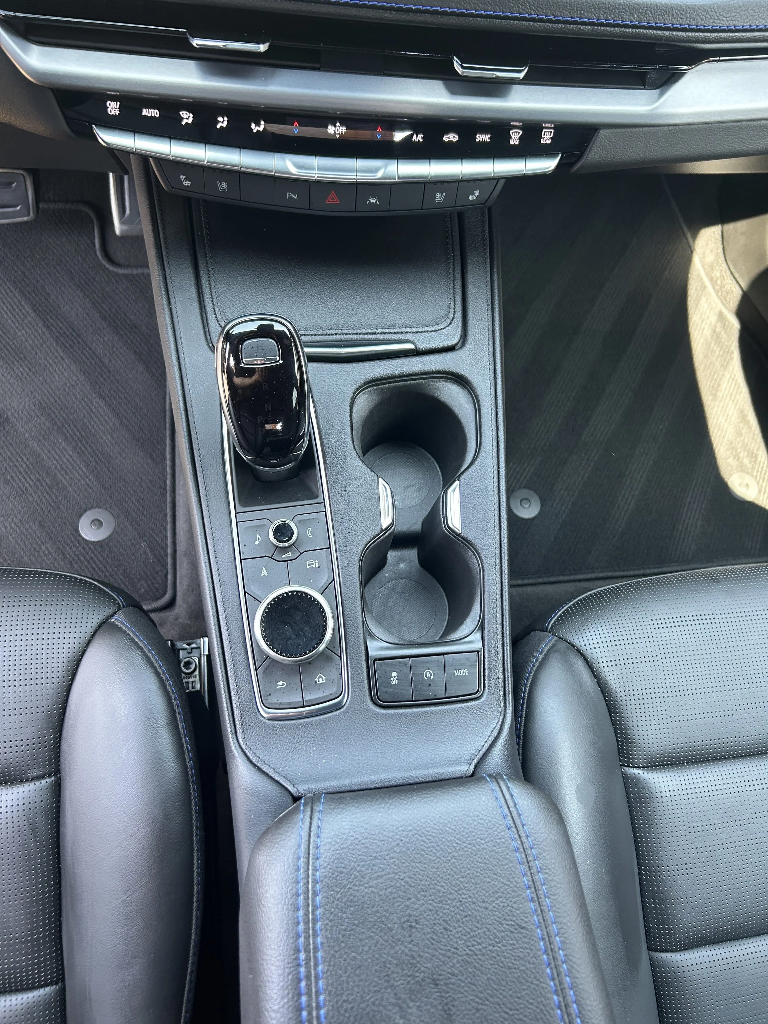 Top view of a car's center console with a gear shift, cup holders, and various controls.