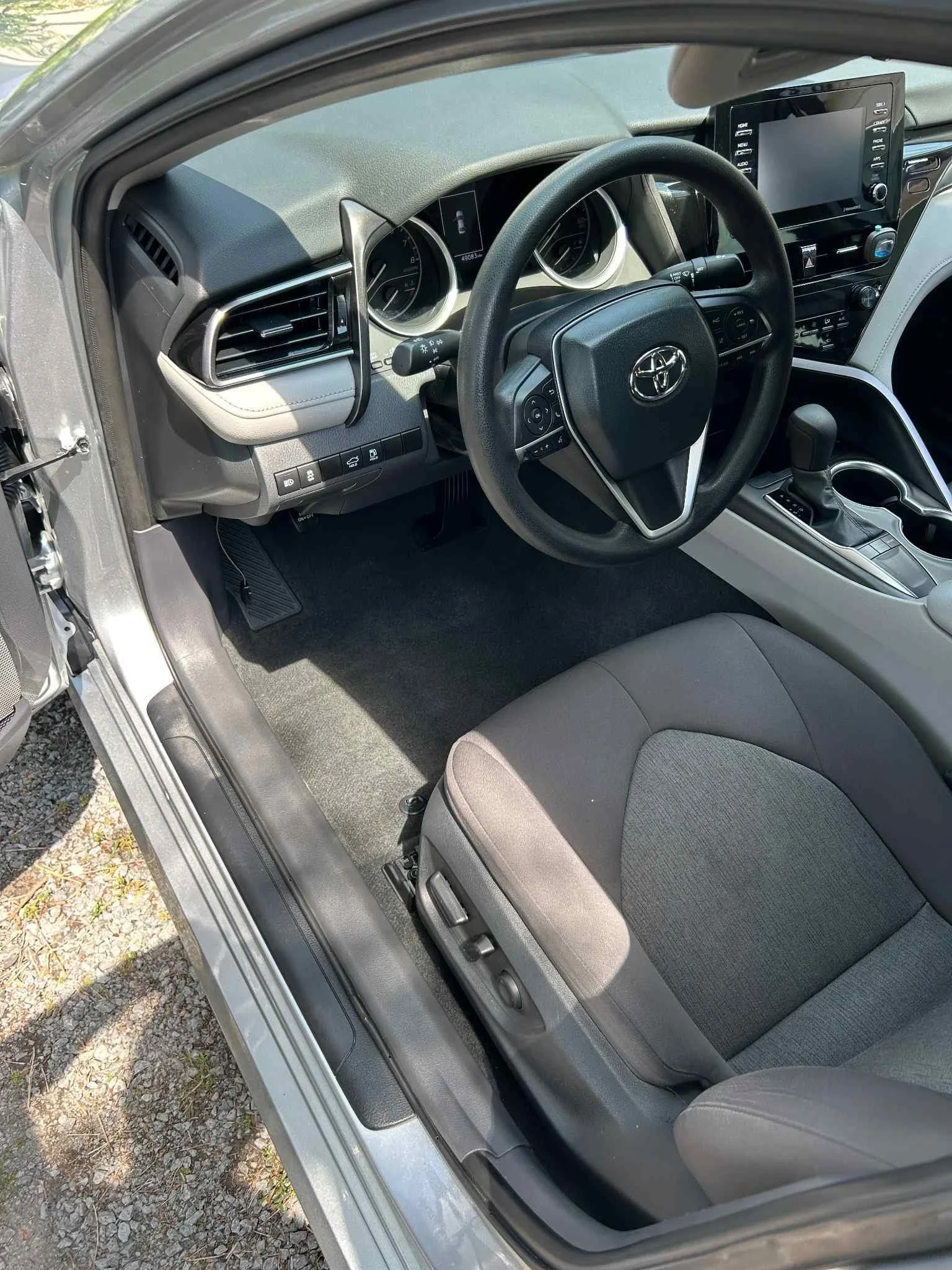 Interior view of a car's driver's seat and dashboard, including steering wheel, gear shift, and infotainment system.