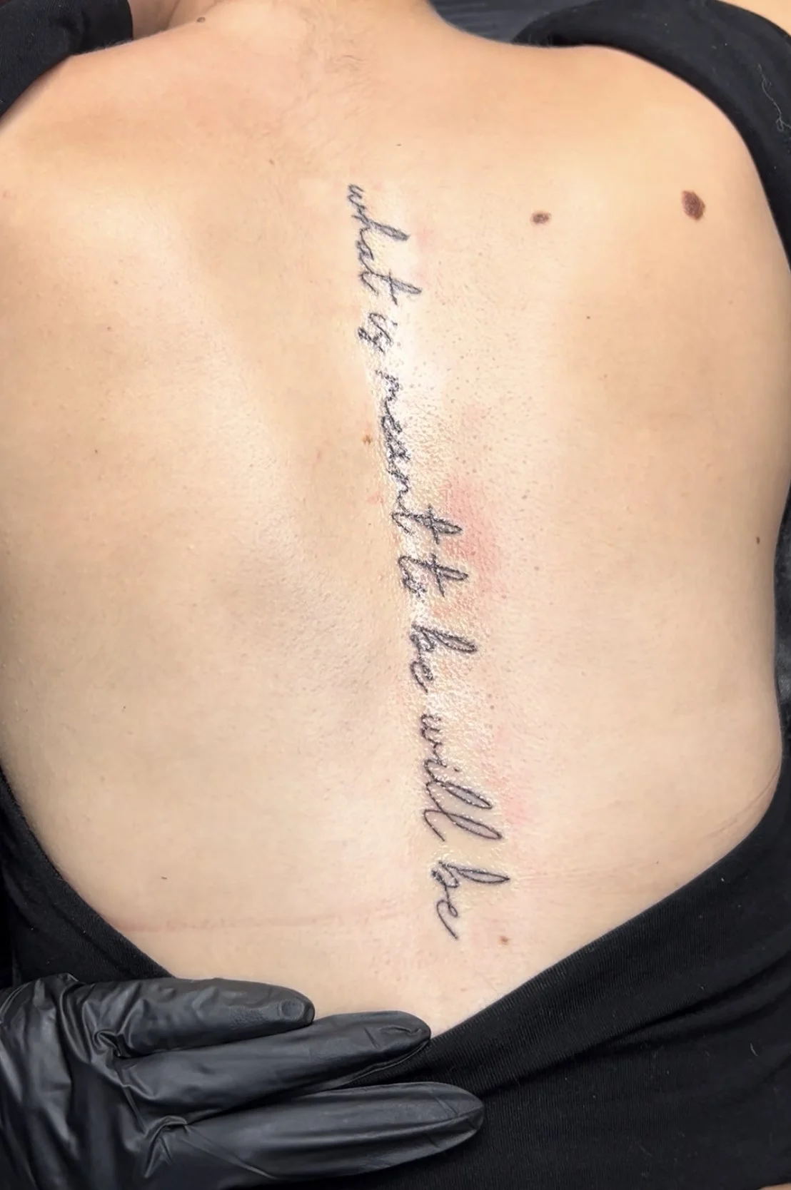 A tattoo on a person's back reads 'My wife is proud of me' in cursive script.