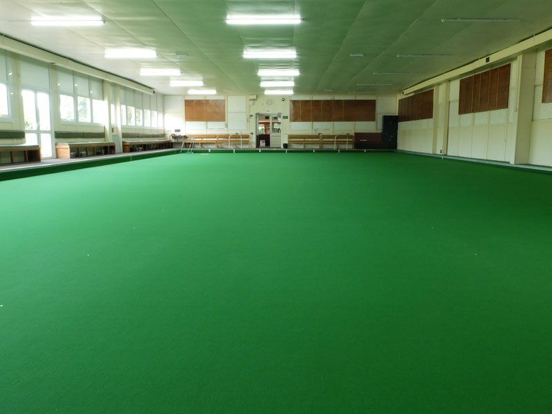 Indoor bowling green with benches, and windows along the side wall.