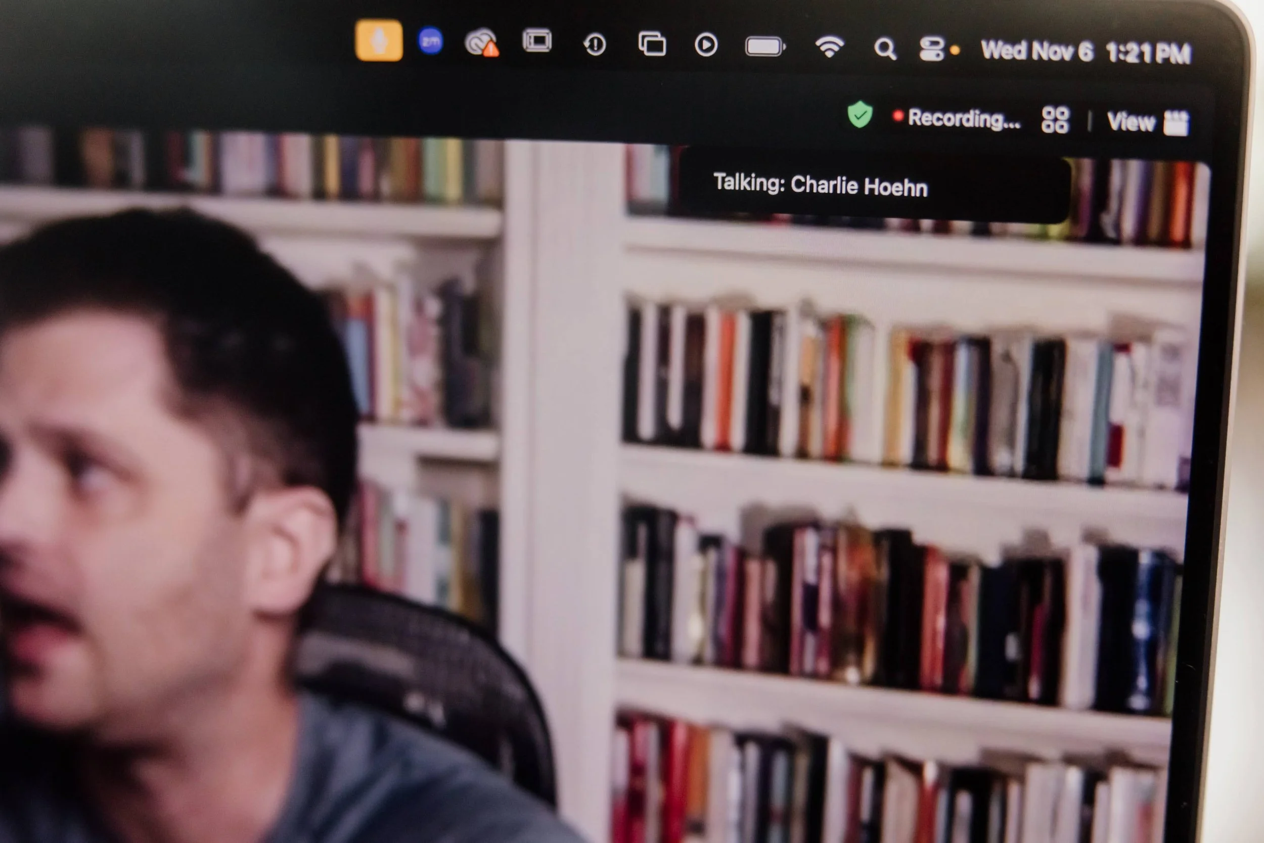 A computer screen showing a video conference in progress with a man with dark hair on the left side, and a background of bookshelves filled with books on the right. The overlay indicates the session is being recorded and the person is talking, identified as Charlie Hoehn. The top right corner displays the date and time: Wed Nov 6, 1:21 PM.