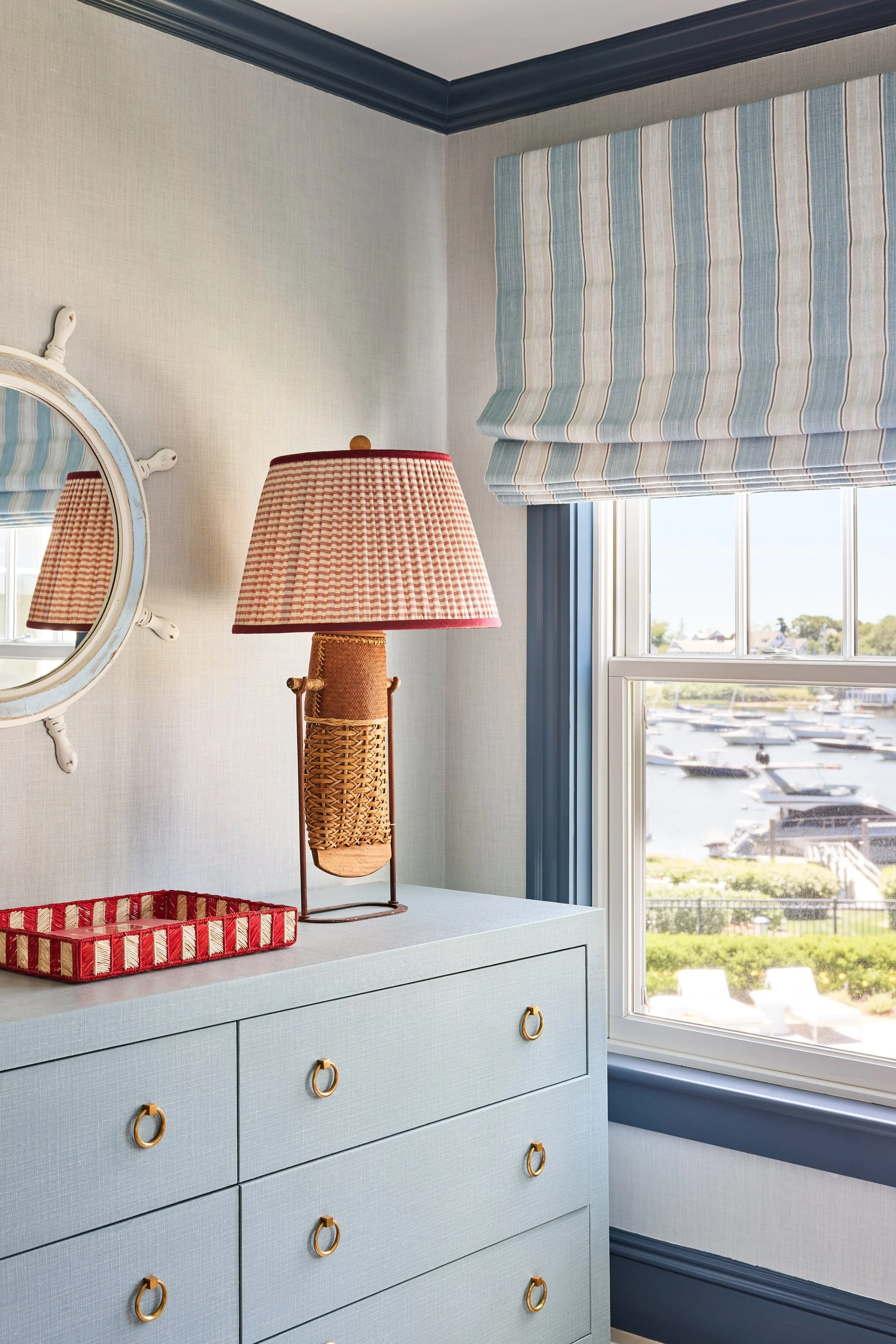Decorative dresser with a wicker lamp, mirror, and window overlooking a marina.