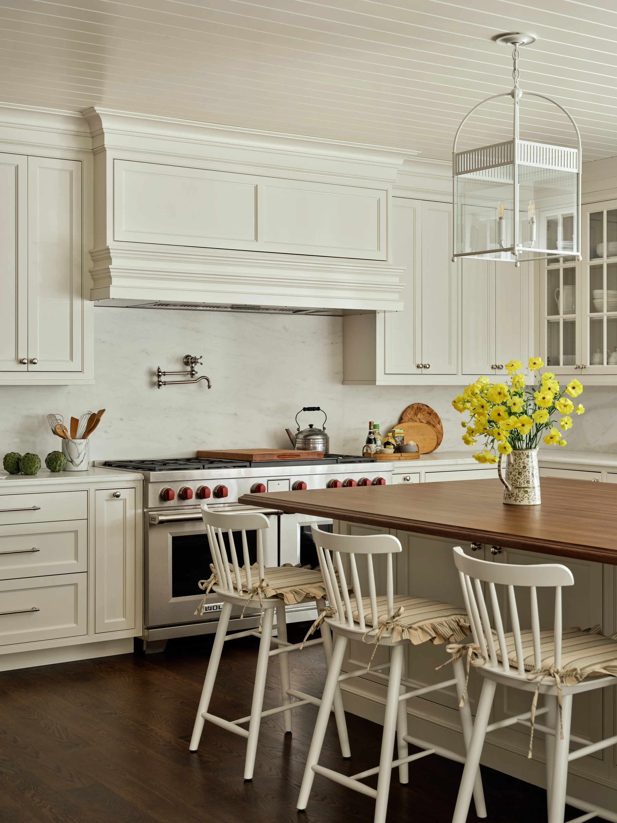 A cozy kitchen with white cabinetry, a wooden island, and a yellow flower bouquet in a patterned pitcher.
