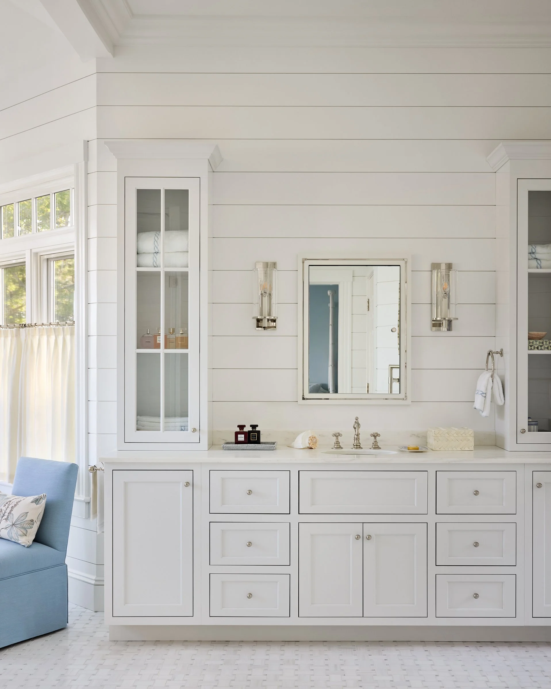 Bright white bathroom vanity with multiple drawers, a mirror, and wall-mounted light fixtures, with a shell and toiletries on the countertop.