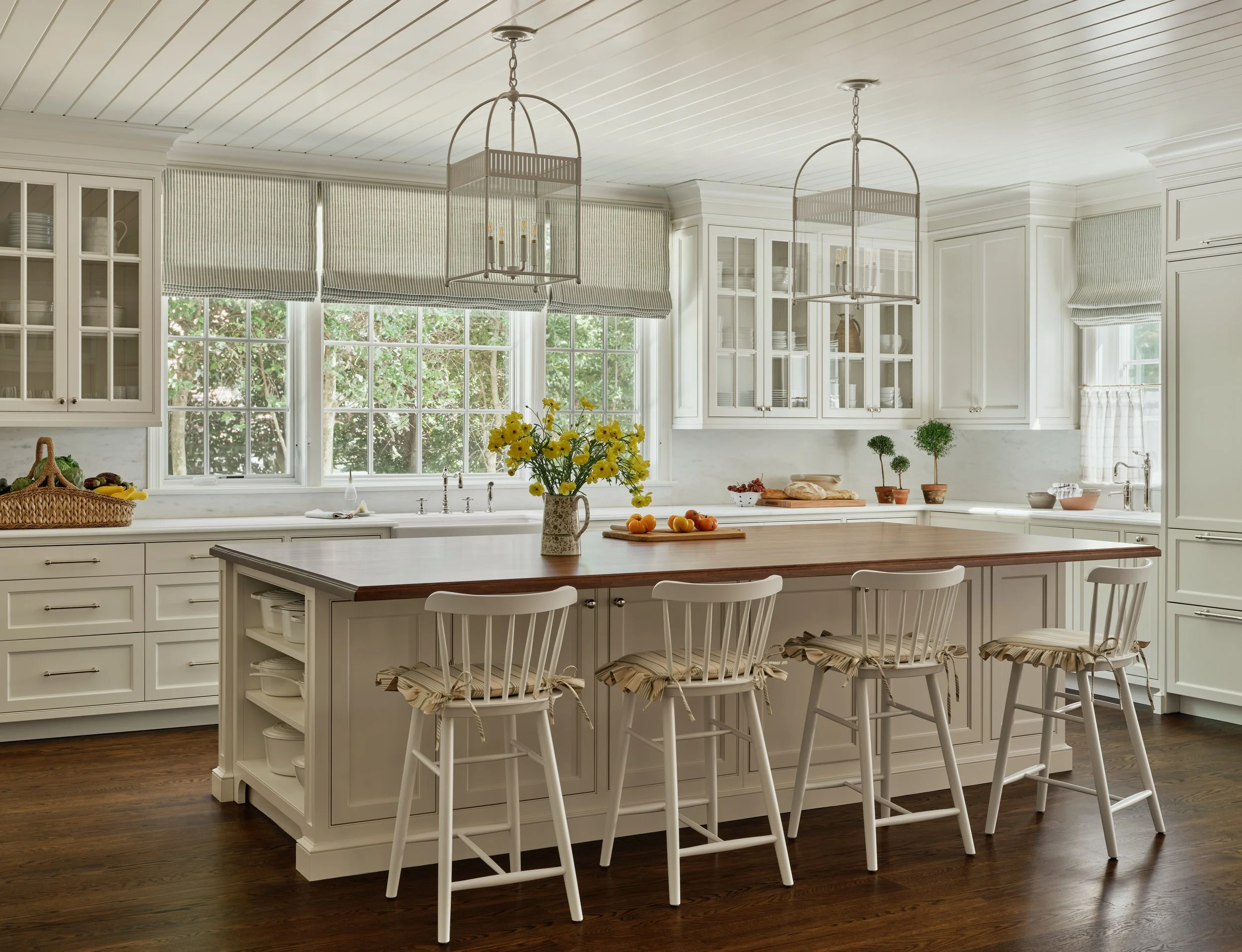 Bright kitchen with white cabinetry, large windows, a wooden island with seating, and hanging light fixtures.