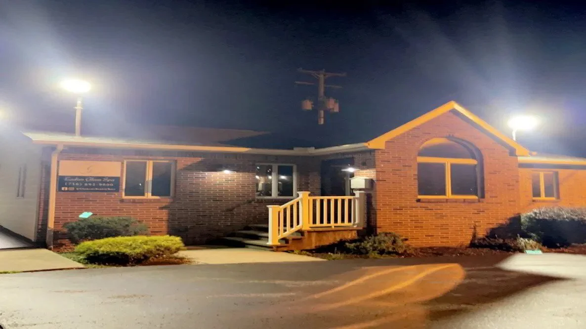 Brick office building at night with lit exterior lights, small front porch, and nearby bushes and parking lot.