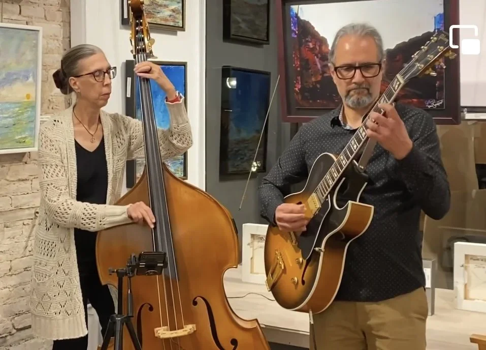 A woman playing a double bass and a man playing an electric guitar in an art gallery.