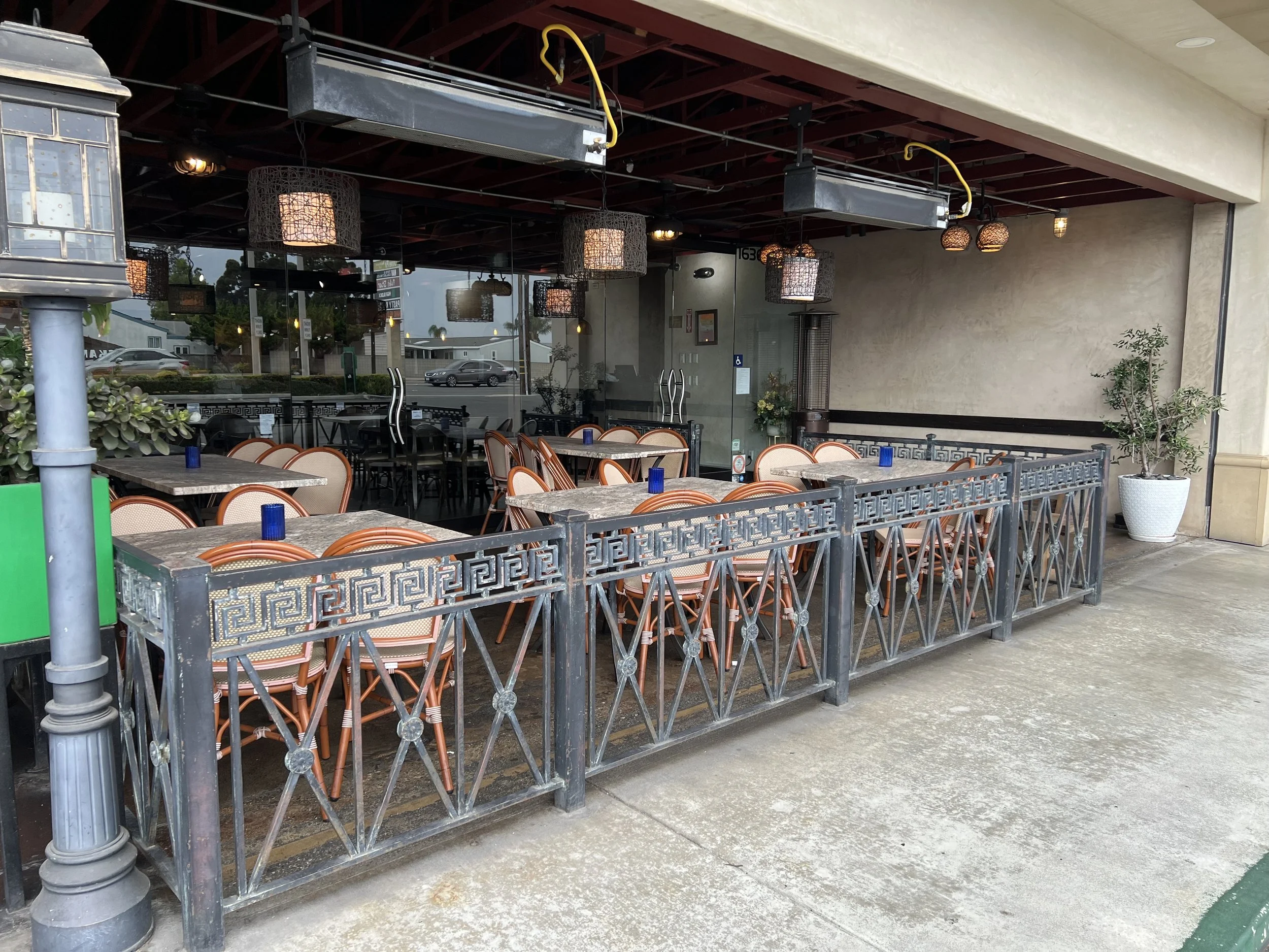 Empty outdoor seating area of a restaurant with tables, chairs, and decorative lighting under a roof with large windowsReflecting street scene with parked cars and buildings