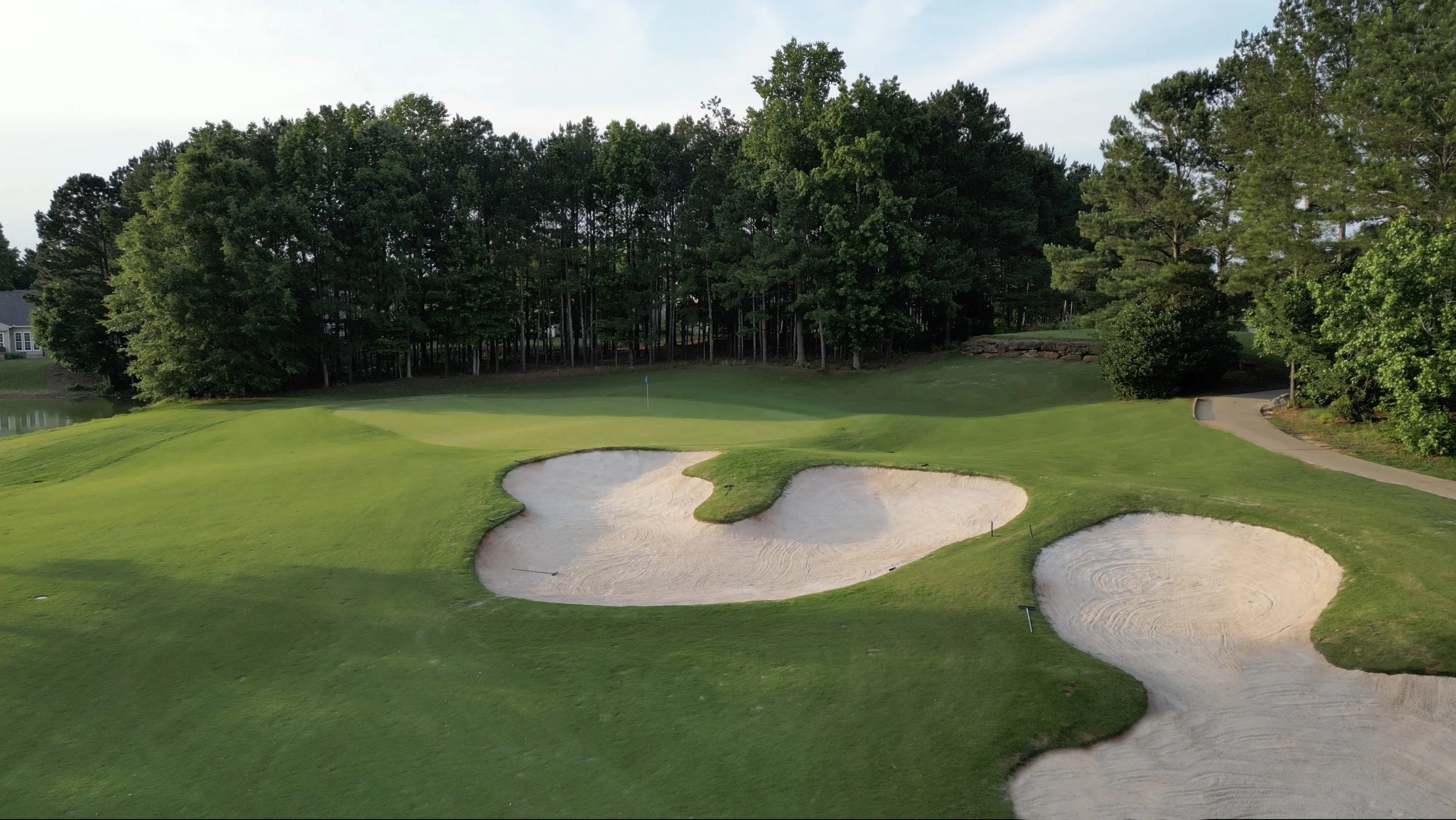 A golf course with a putting green, sand bunkers, and surrounding trees.