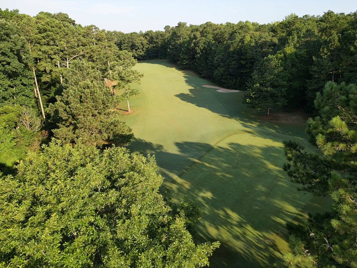 Aerial view of a golf course fairway surrounded by dense trees, with a sand trap visible on the right side.