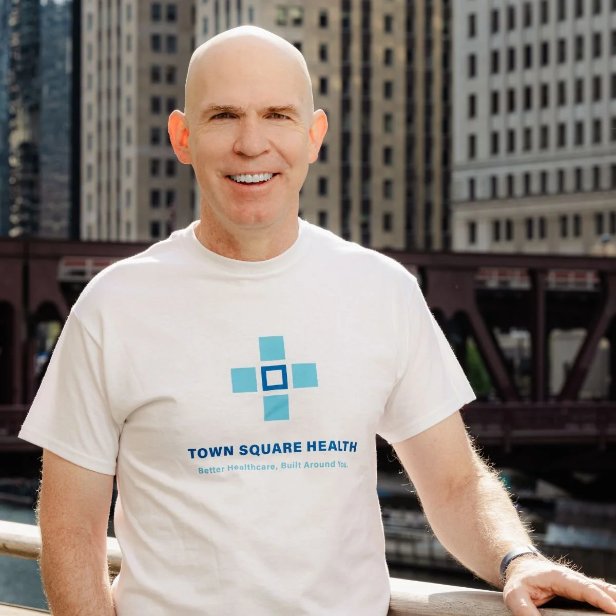 Image of Dr. David Buchanan, a smiling white man, in a Town Square Health t-shirt standing in front of the Chicago river and buildings