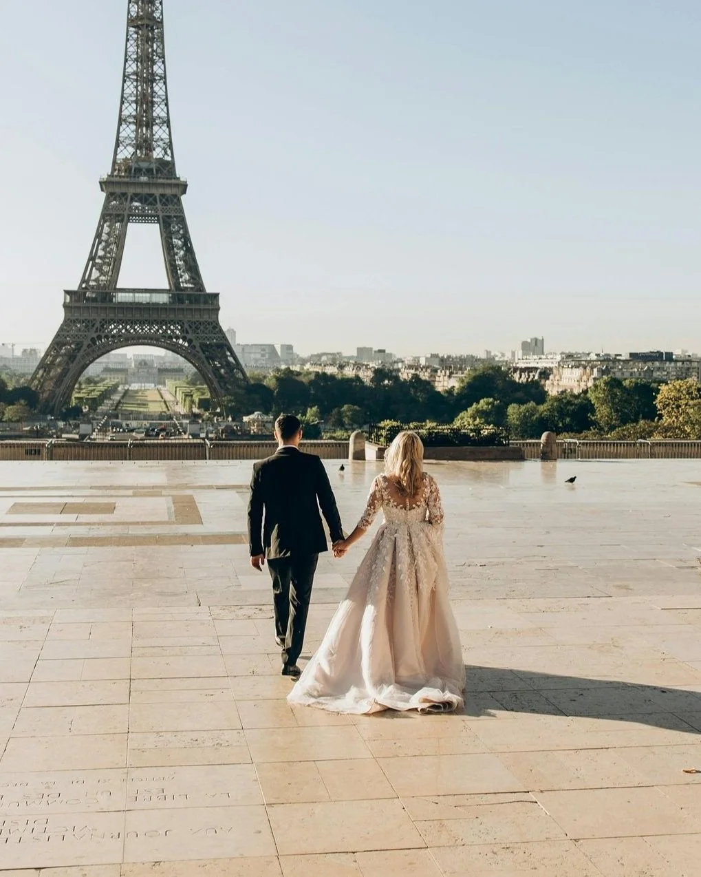 A bride and groom holding hands and walking towards the Eiffel Tower in Paris, France, during daytime.