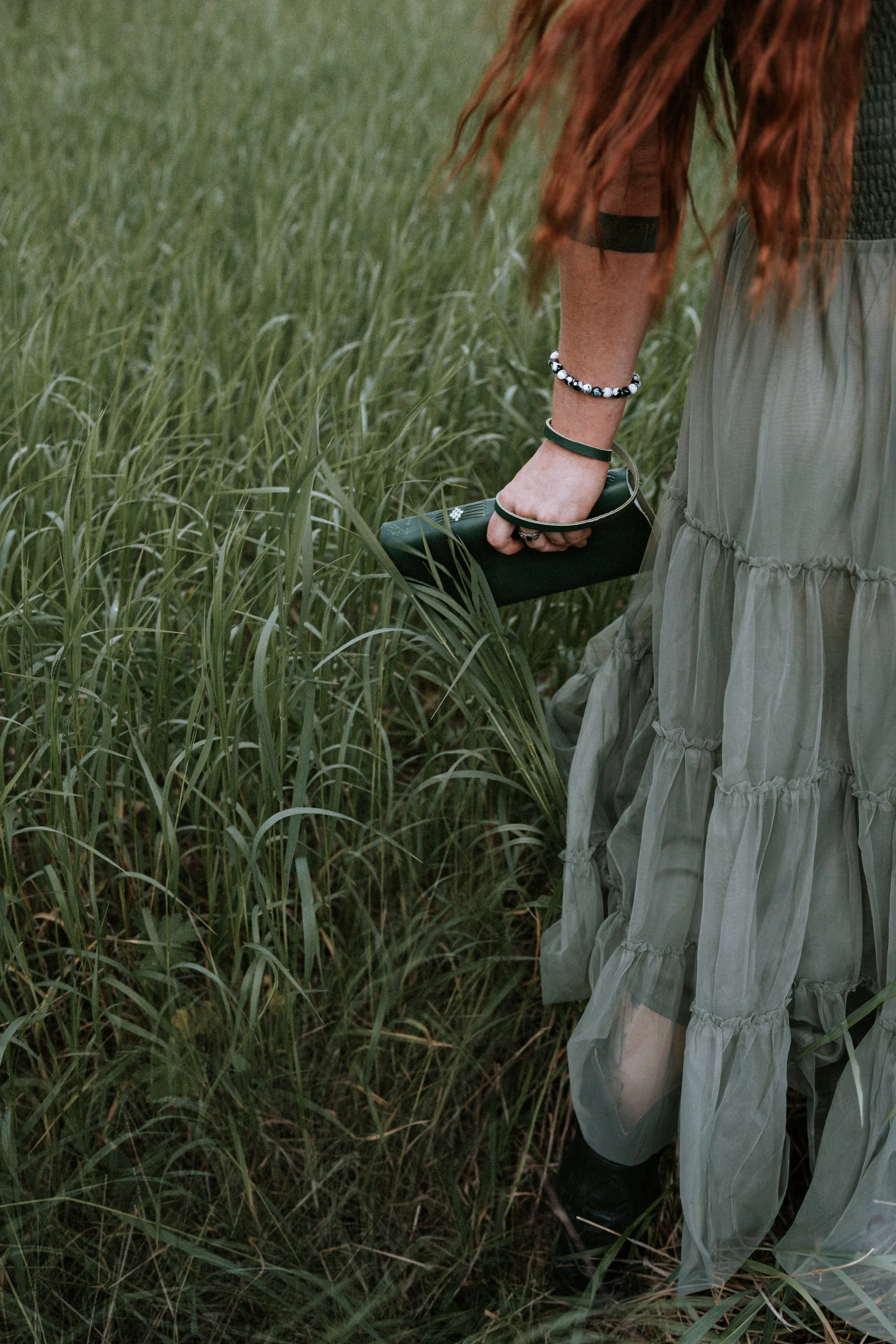 Person holding a green notebook in a grassy field, wearing a long green dress, and bracelets Montana editorial portrait photographer.