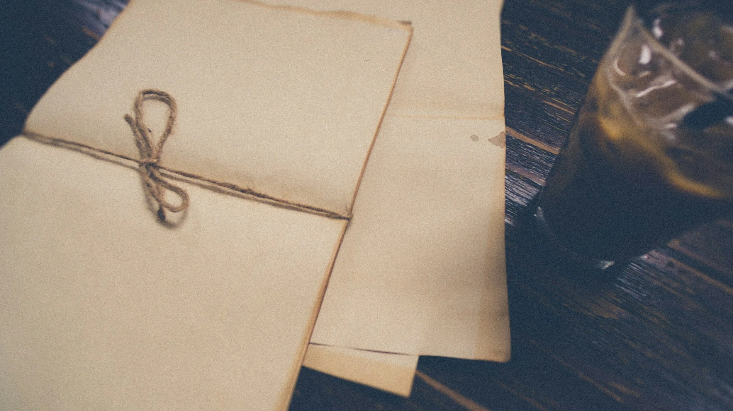 A bundle of letters tied with twine resting on a wooden desk