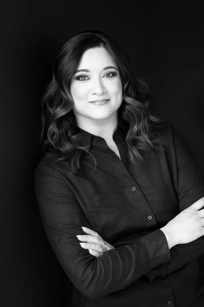 Black and white photo of Daphne smiling wearing a button up shirt against a solid backdrop.