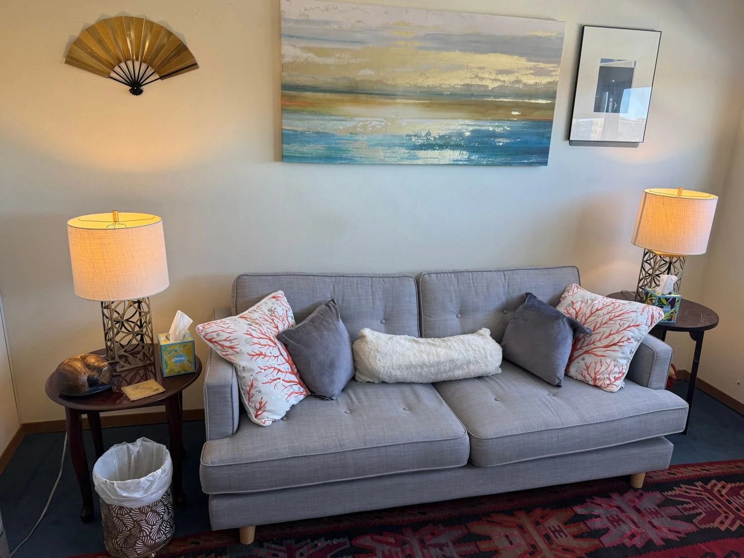 A grey couch with throw pillows against a wall with an abstract blue and grey painting above it.