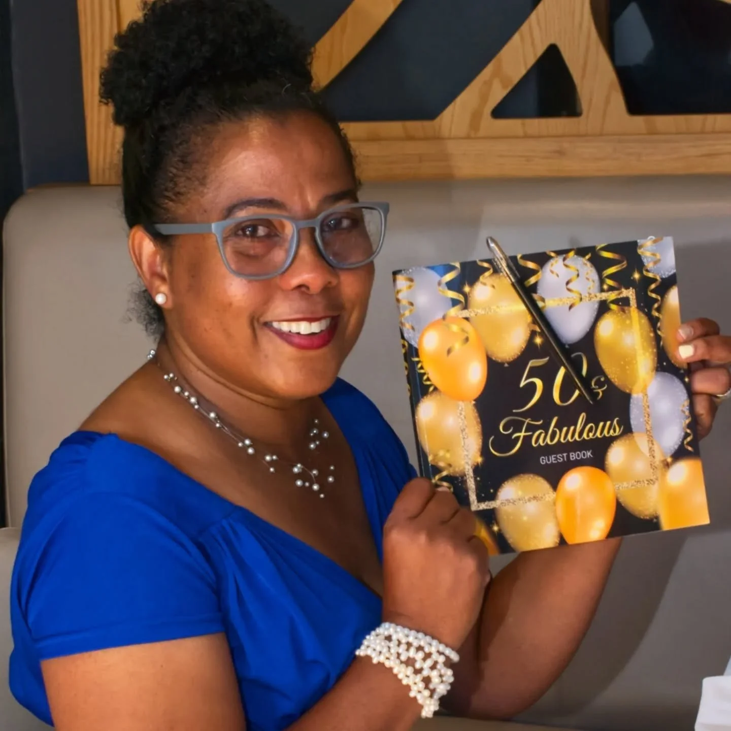 &quot;Fifty &amp; Fabulous&quot;
A shimmer of years  in her hands,
Golden balloons echoing laughter past.
Pearls trace the rythm of memory
Sift-spoken, resilient,
A guest of her own becoming.
She sits where joy gathers,
Blue as twilight,
Fabulous as 