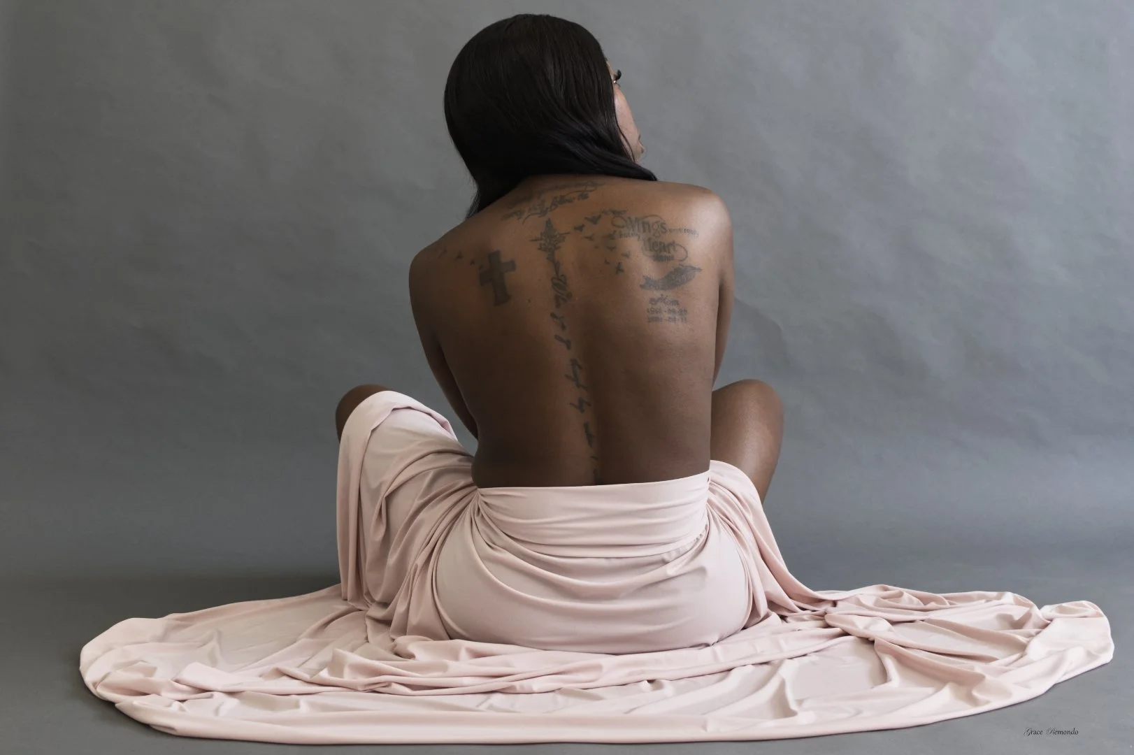 Looking out a window, her tattoos from her spine to her upper back and shoulders reveal her steadfastness and resilience. She is at home in her body.
