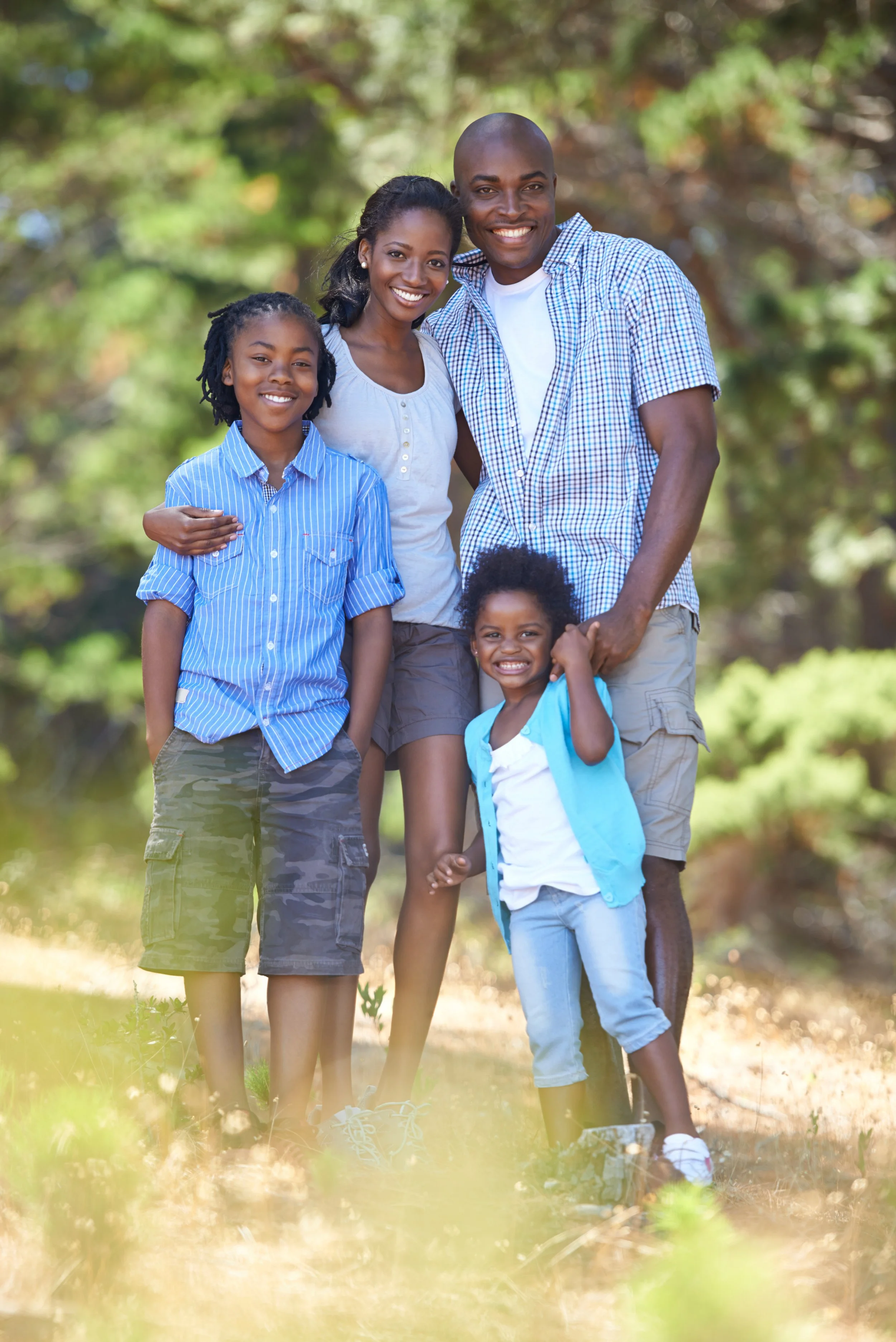 A happy multigenerational African American family of five outdoors in a wooded area, smiling and posing for a photo.