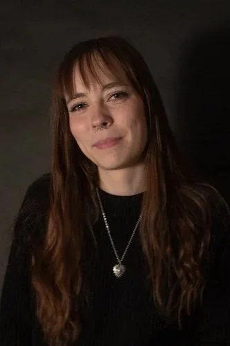 Smiling young woman with long hair and bangs, wearing black.