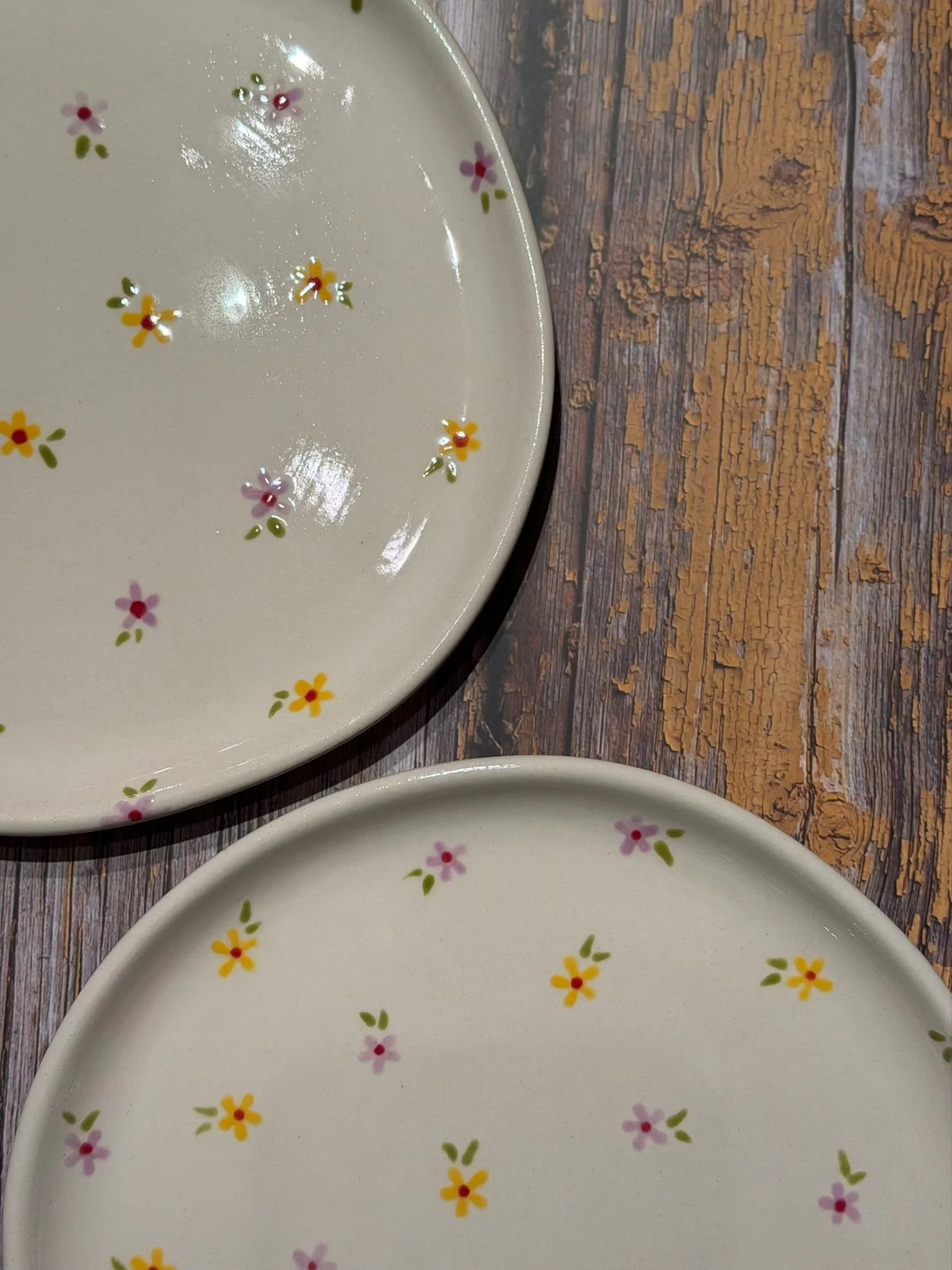 Zwei cremefarbene Keramikteller mit kleinen gelben und rosafarbenen Blumen auf einer verwitterten Holzoberfläche