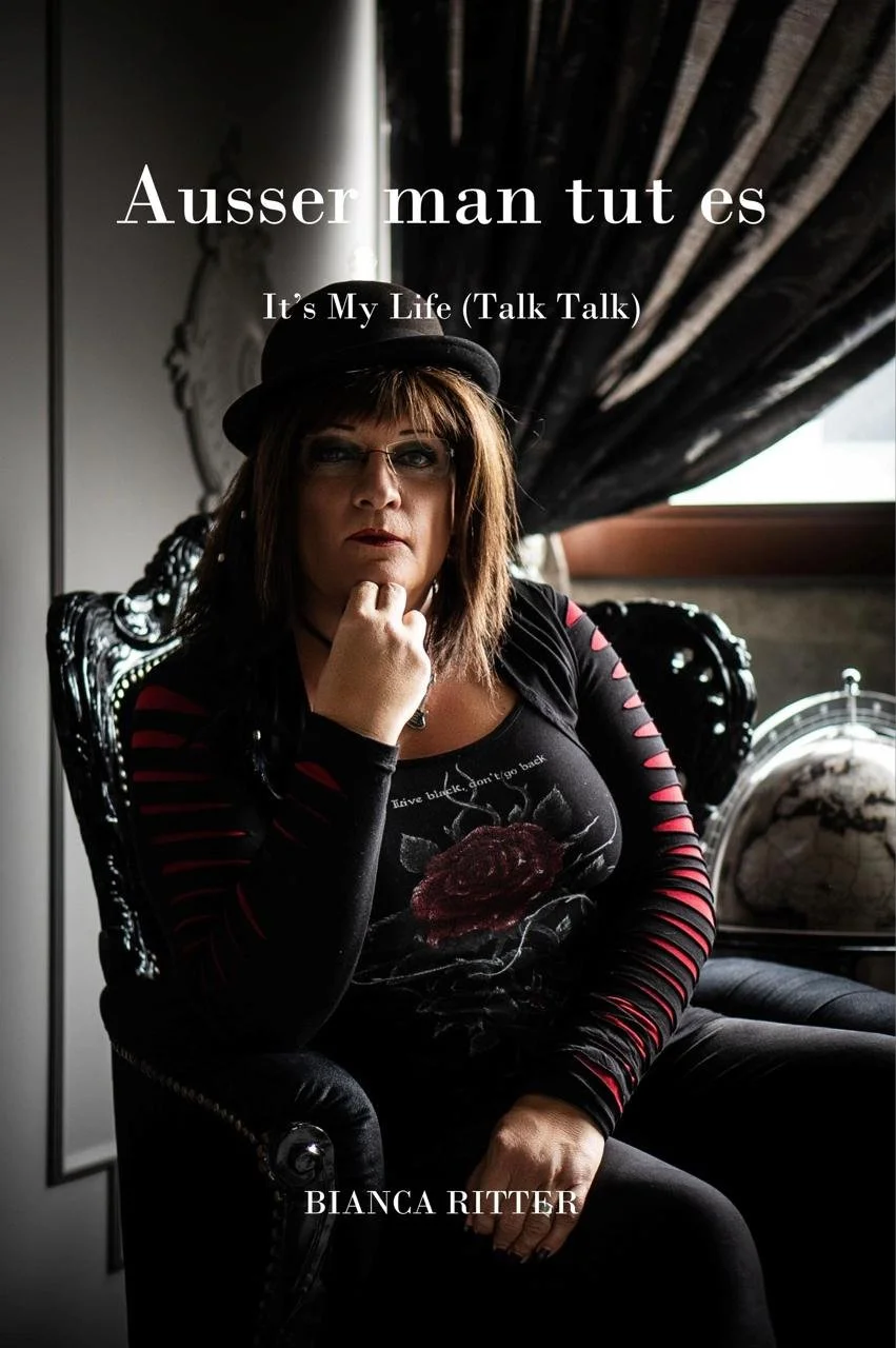 Person mit Hut und Brille sitzt in dunklem Ohrensessel, Hand am Kinn, im Hintergrund Vorhang und Globus Text auf Bild: Ausser man tut es – It's My Life (Talk Talk), Bianca Ritter