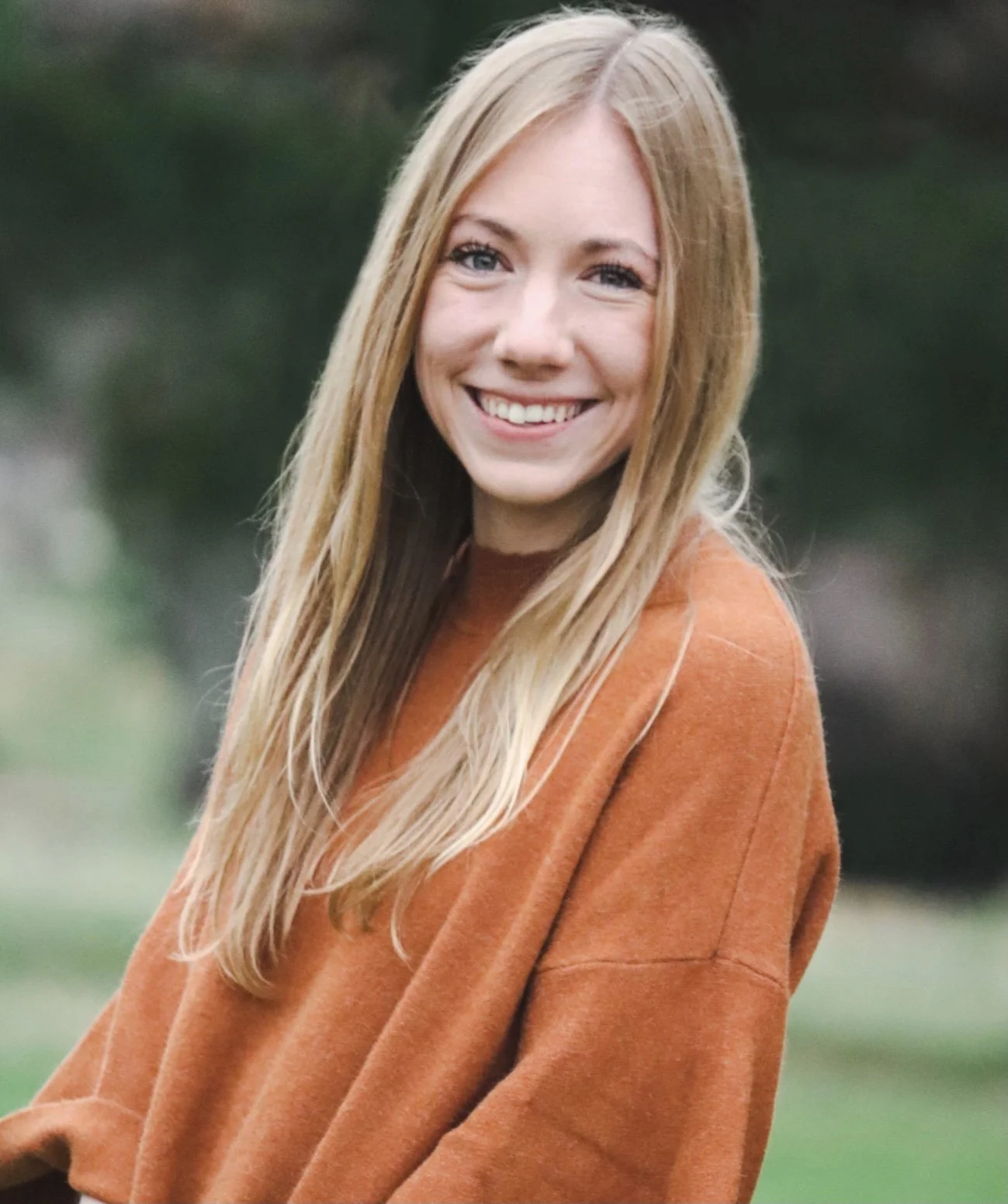 Haley, founder of Forge + Field Co., smiling outdoors in a rust-colored sweater – leadership coach and strategic guide for mission-driven teams, nonprofits, and camps.