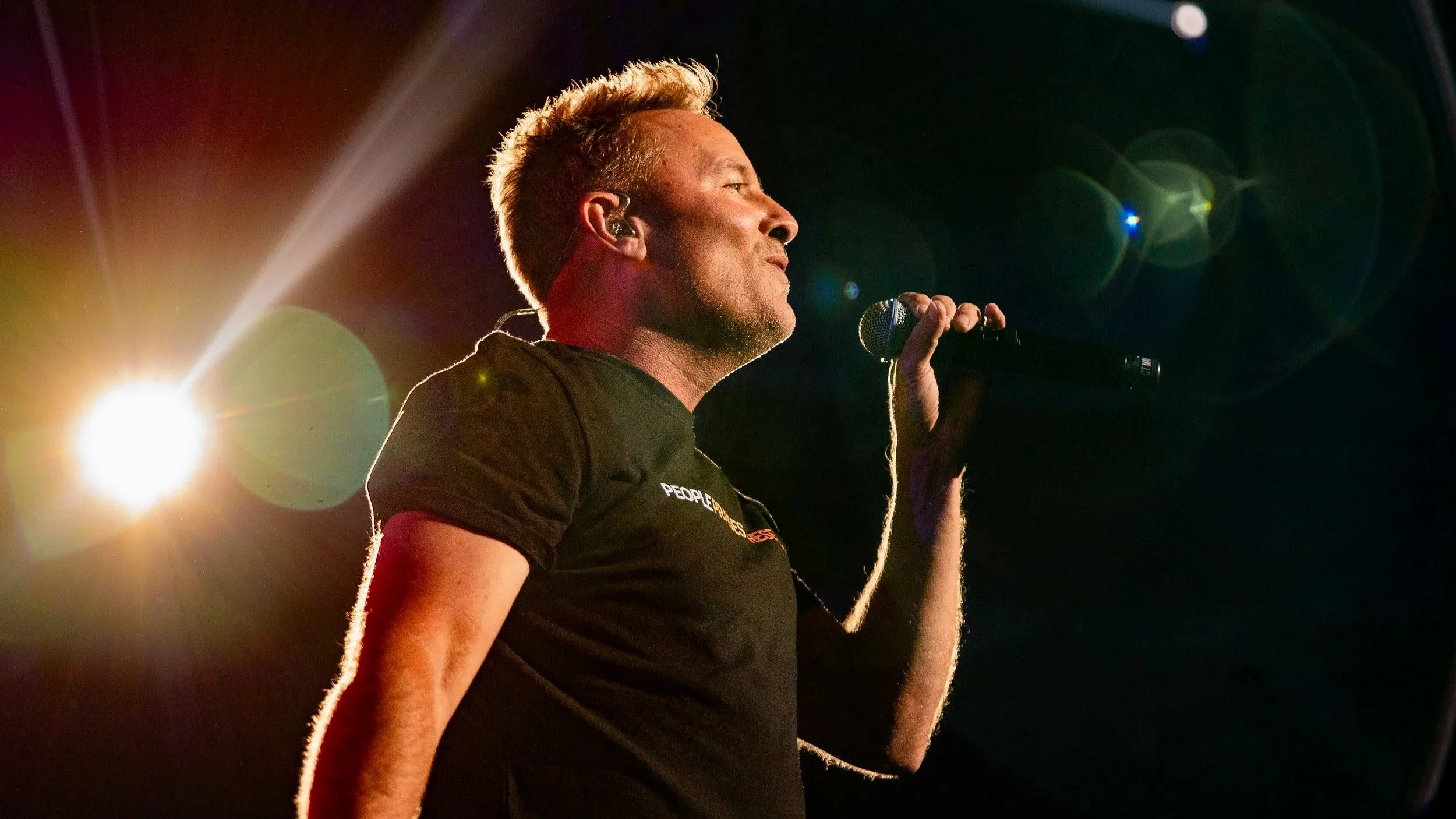 Christian music star, Chris Tomlin, singing into a microphone on stage, with bright stage lights and lens flare effects.
