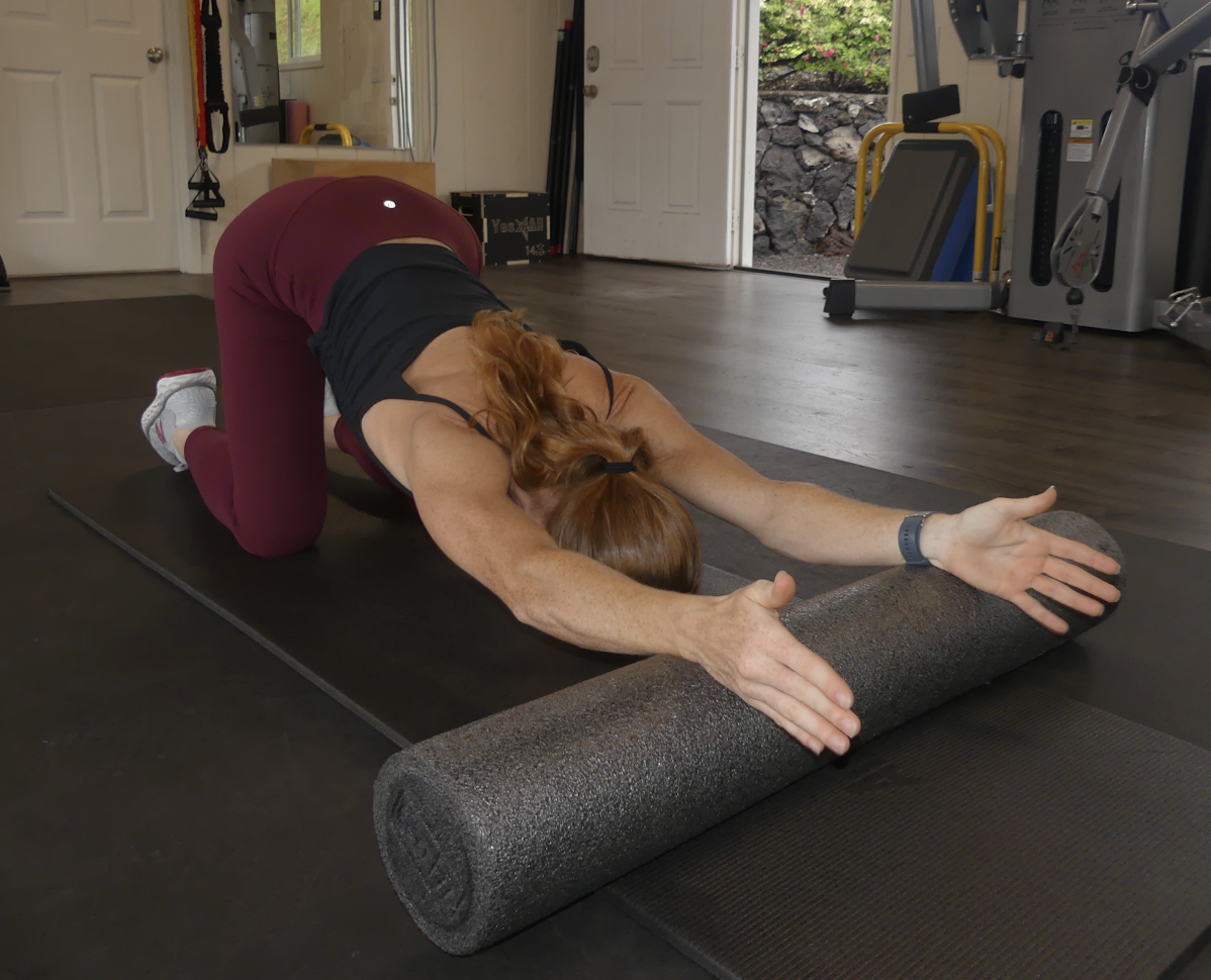 A woman performing a stretching exercise on a yoga mat at a private fitness studio, using a foam roller for stretching her back.