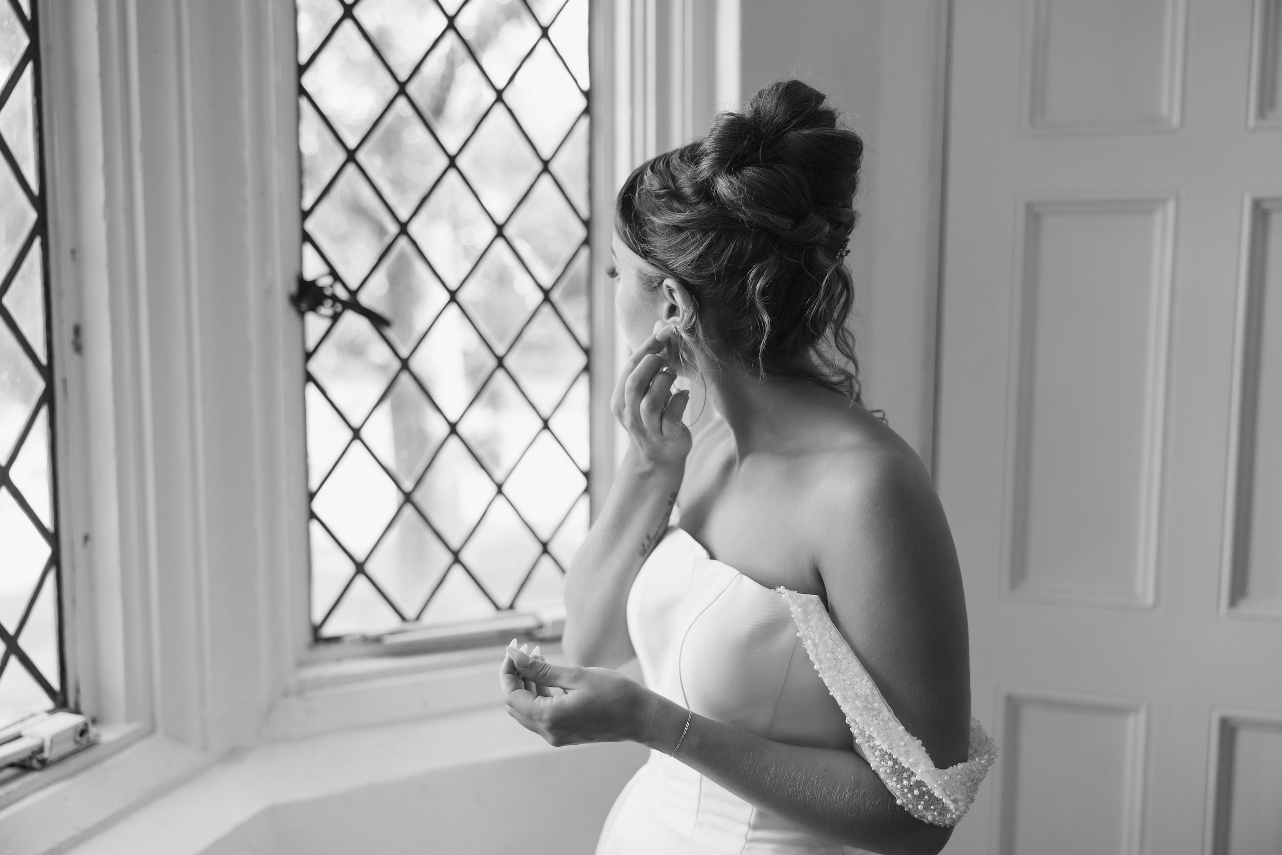 A bride fixing her earring near a window at the Pinecroft wedding venue at Crosley Estate Cincinnati Ohio