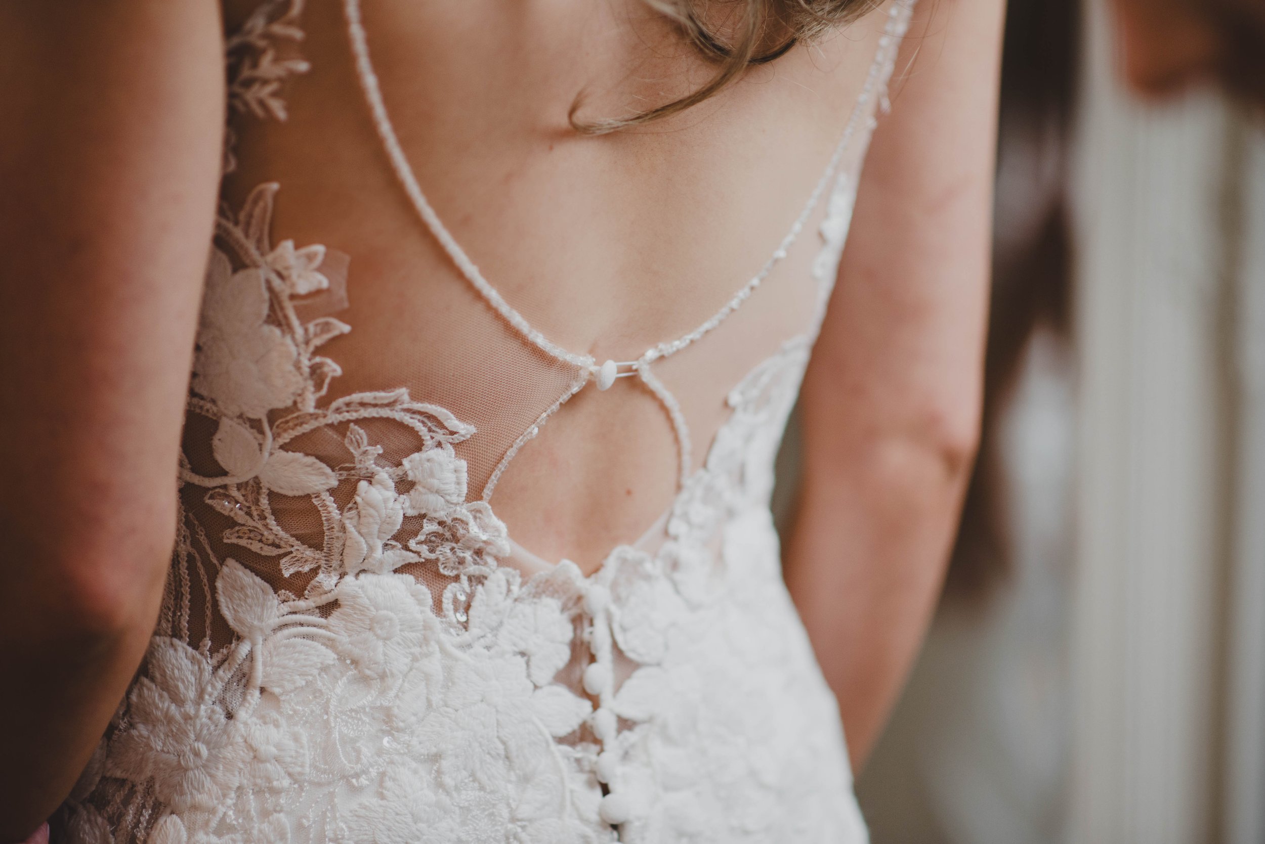 Close-up of a bride wearing a white lace wedding dress with intricate floral embroidery and a delicate necklace.