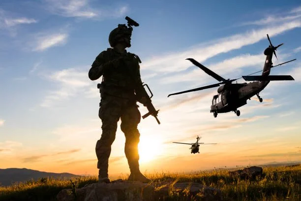 Silhouette of a soldier holding a rifle with two helicopters flying in the sunset sky