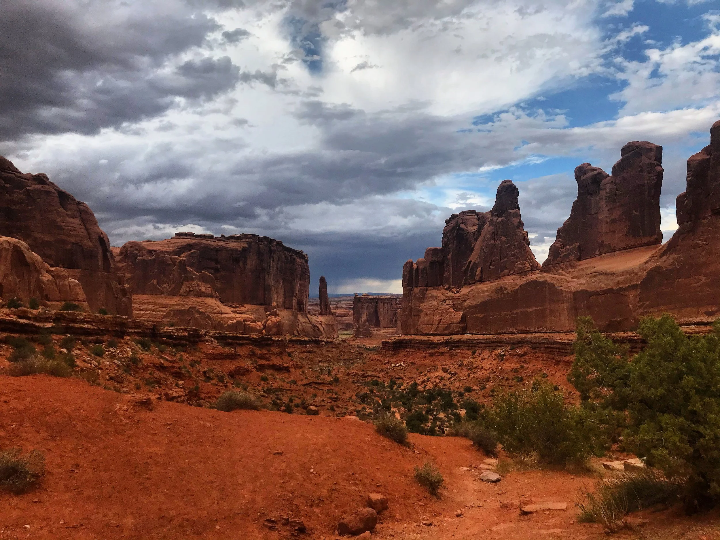 Red rock formations and cliffs in a desert landscape under a cloudy sky.
