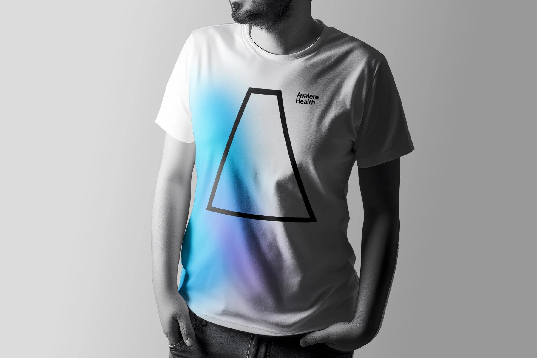 Gray T-shirt with a black outlined abstract shape and the text 'Avalere Health' on the chest, worn by a man with his hands in his pockets, against a gray background.