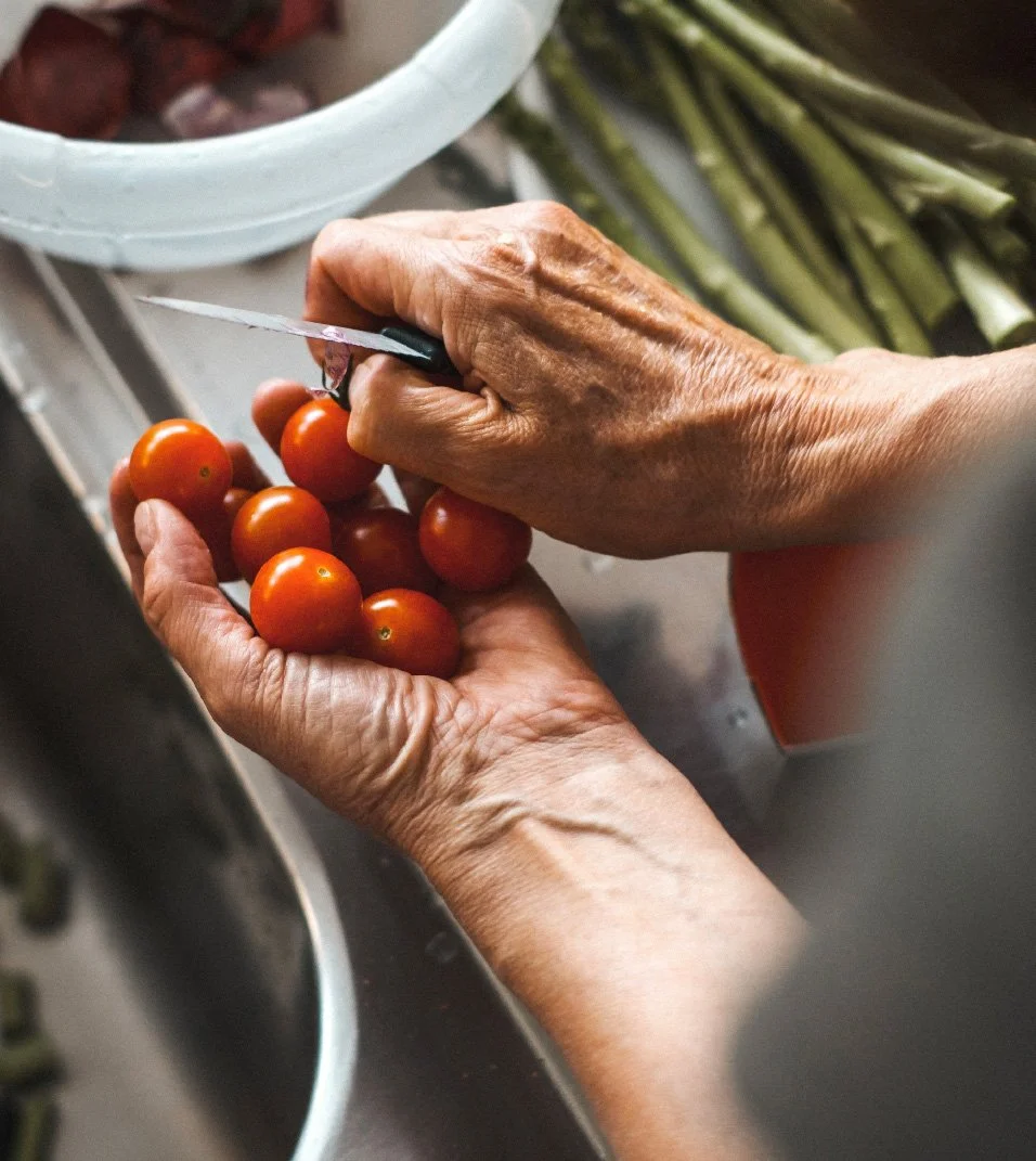 Elderly woman cutting tomatoes as she prepares a meal in her kitchen