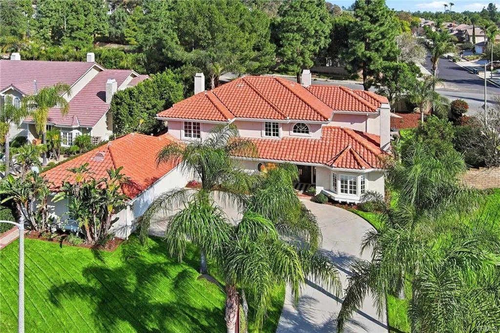 A large house with a red tiled roof, surrounded by palm trees and green lawn, situated in a suburban neighborhood.