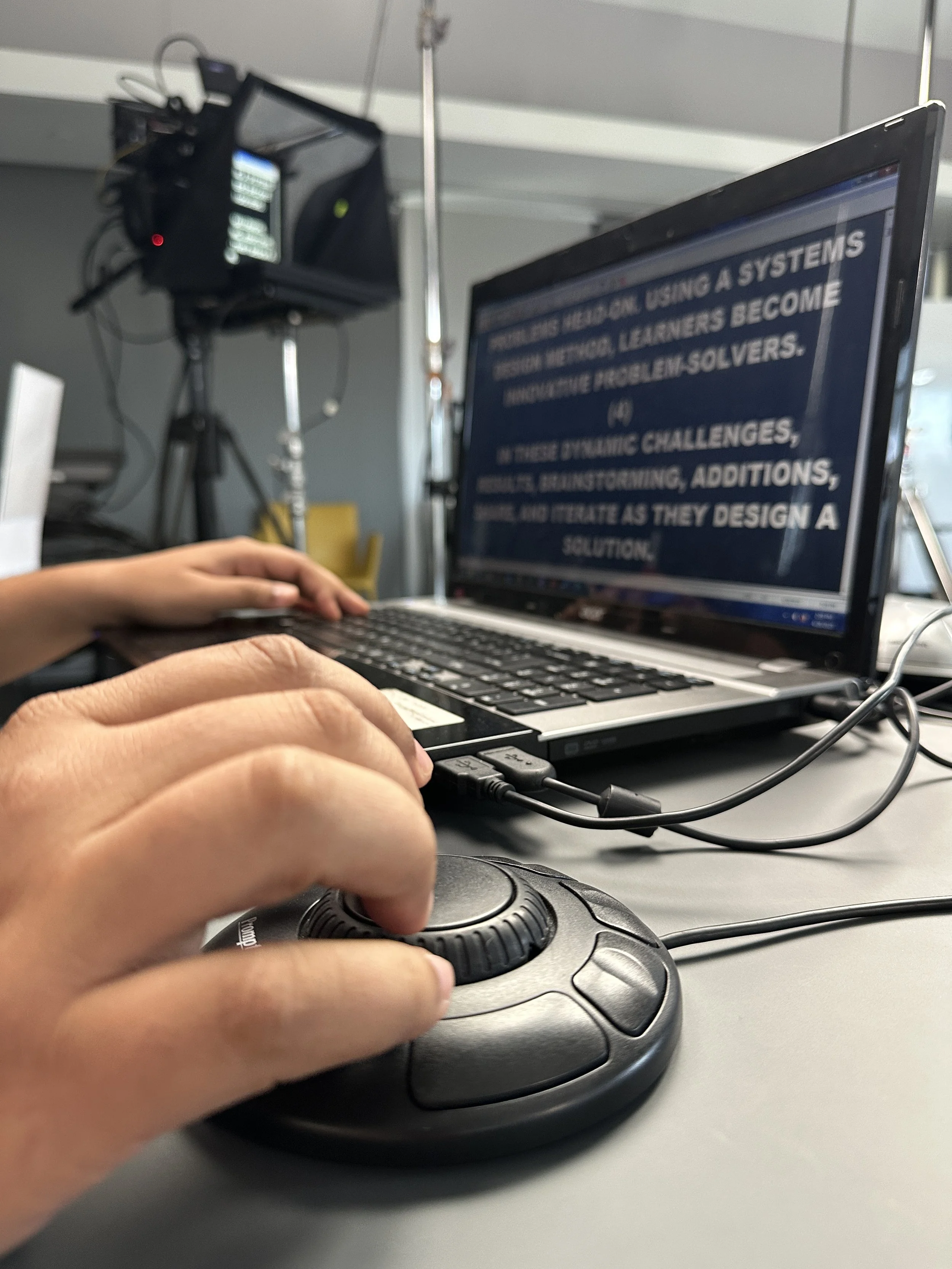 Person using a computer mouse at a desk with a laptop displaying a teleprompter presentation.