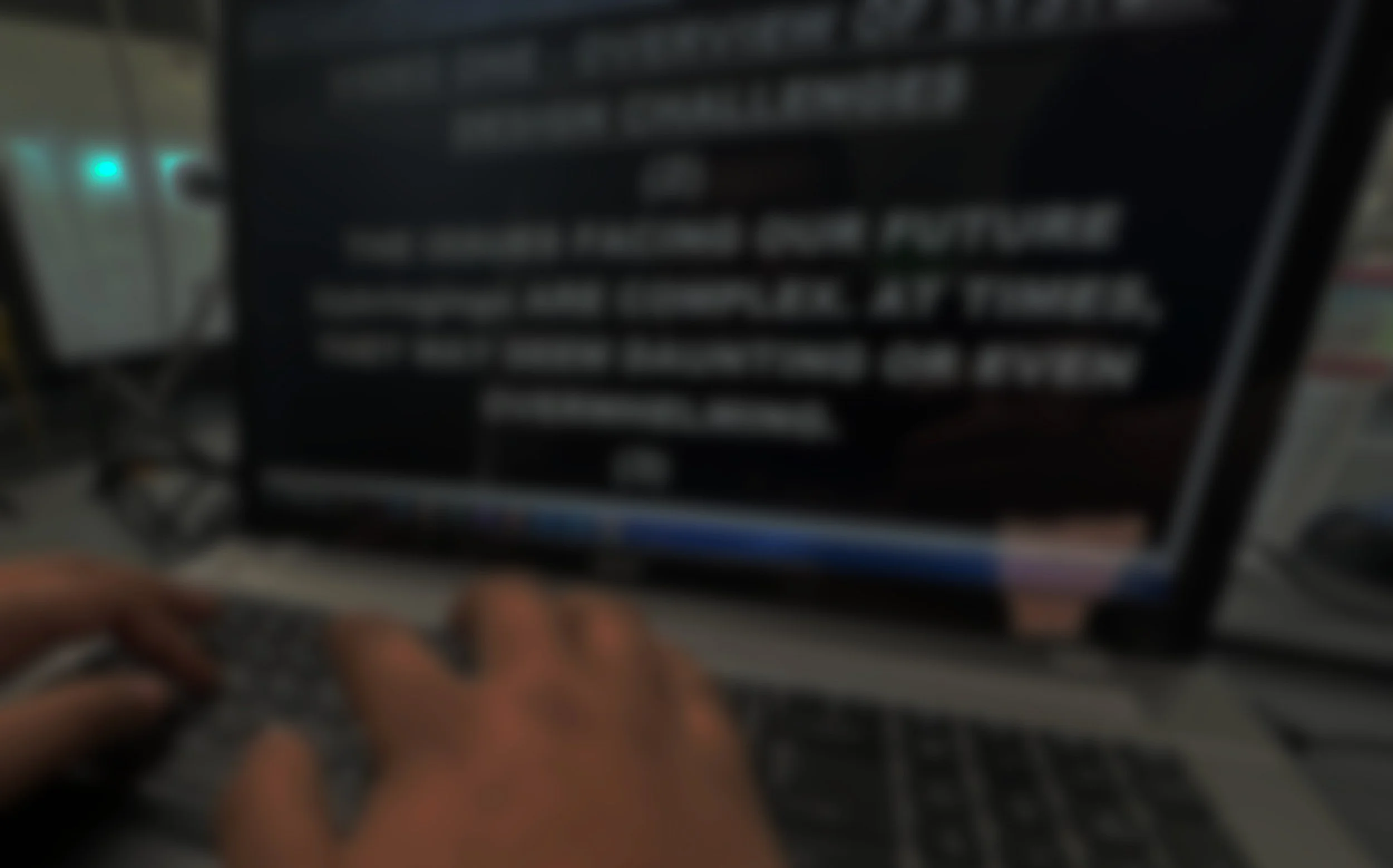 A person typing on a keyboard in front of a computer monitor displaying blurred text.