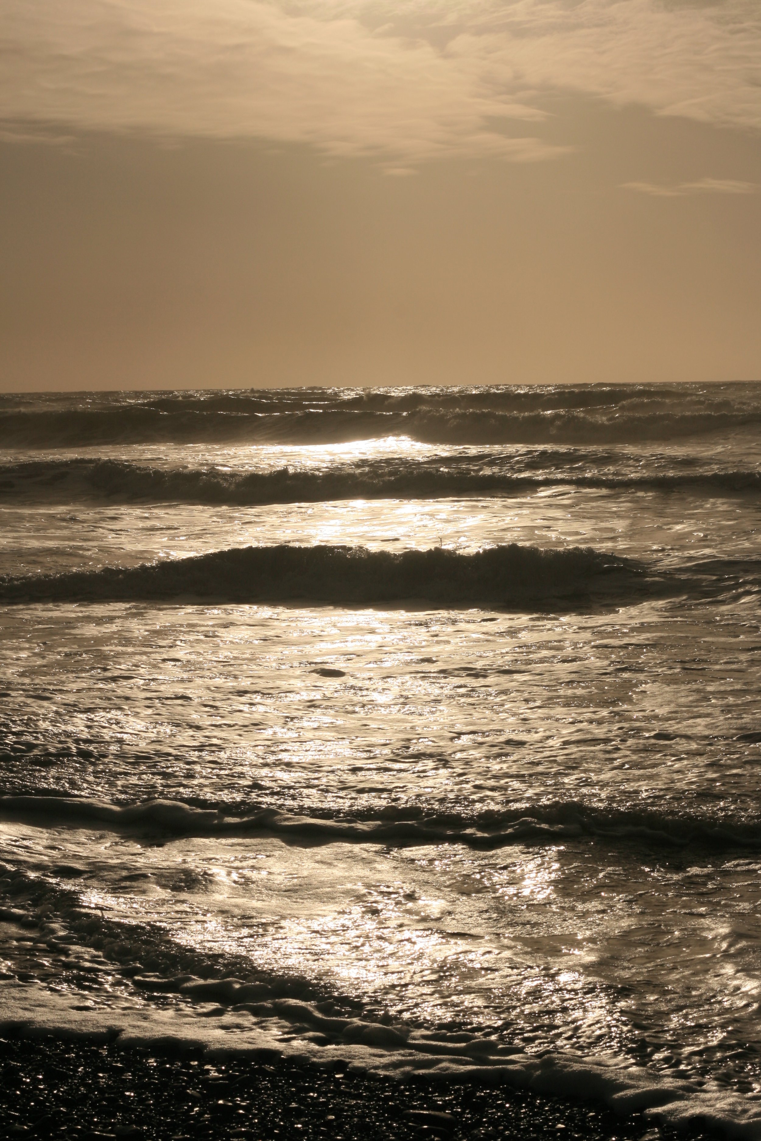 Sunset over the ocean with gentle waves reflecting the golden light, partly cloudy sky.