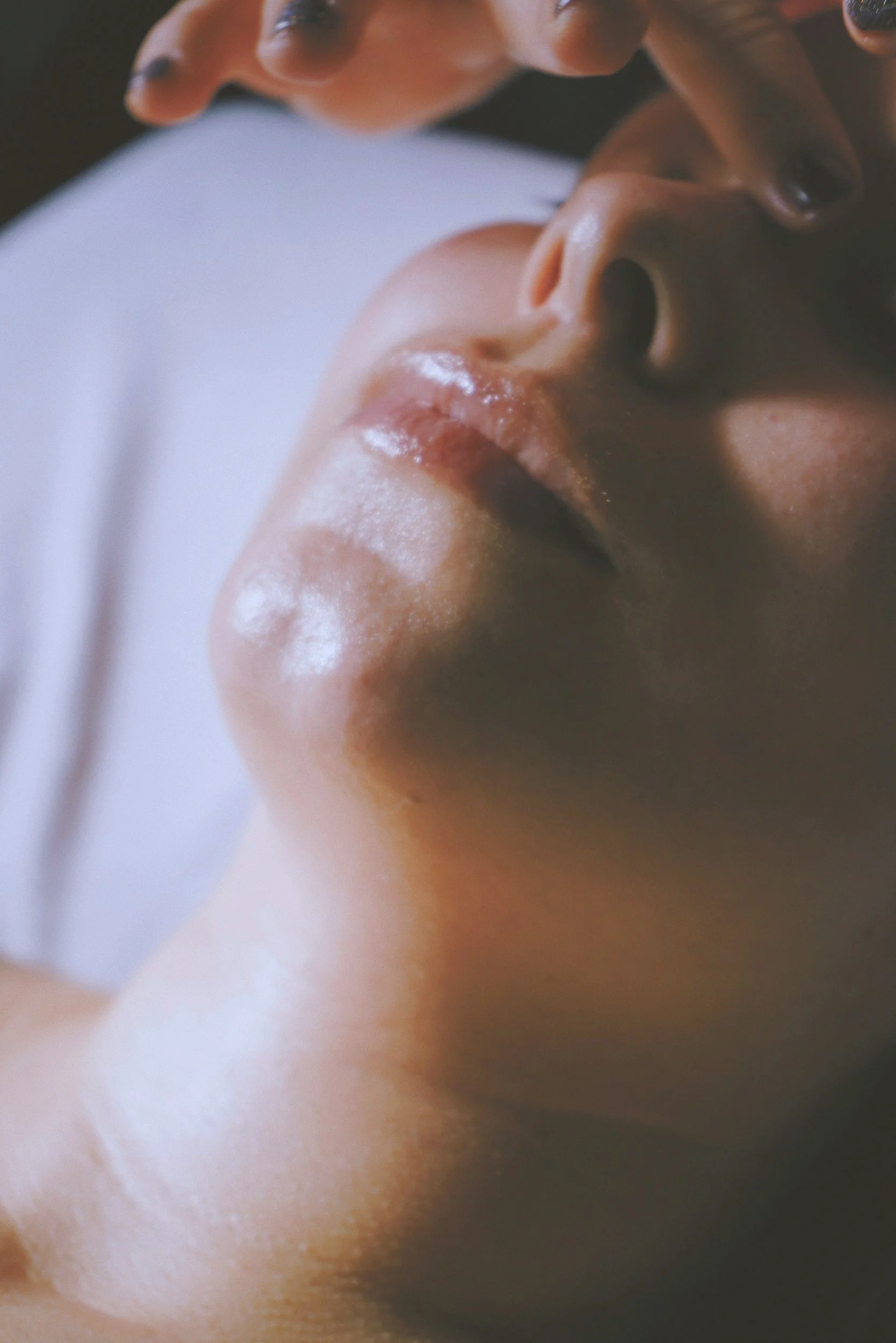 Close-up of a person's face with eyes closed, lying down, with one hand gently touching their forehead, showing a serene expression.