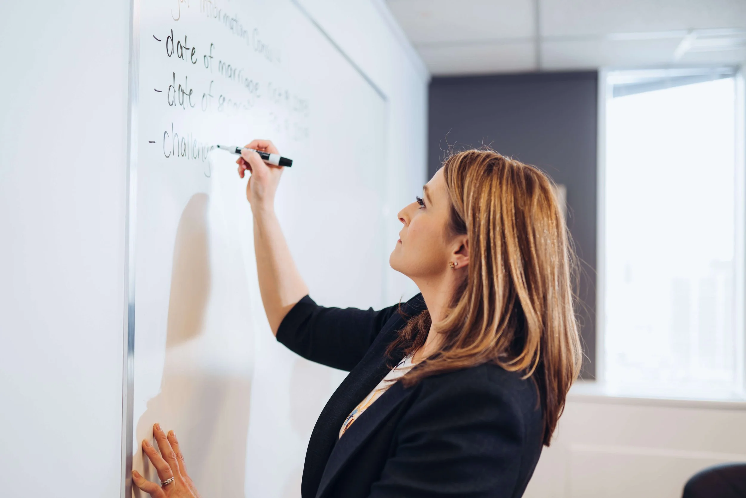 A woman writing on a whiteboard in a classroom or meeting room.