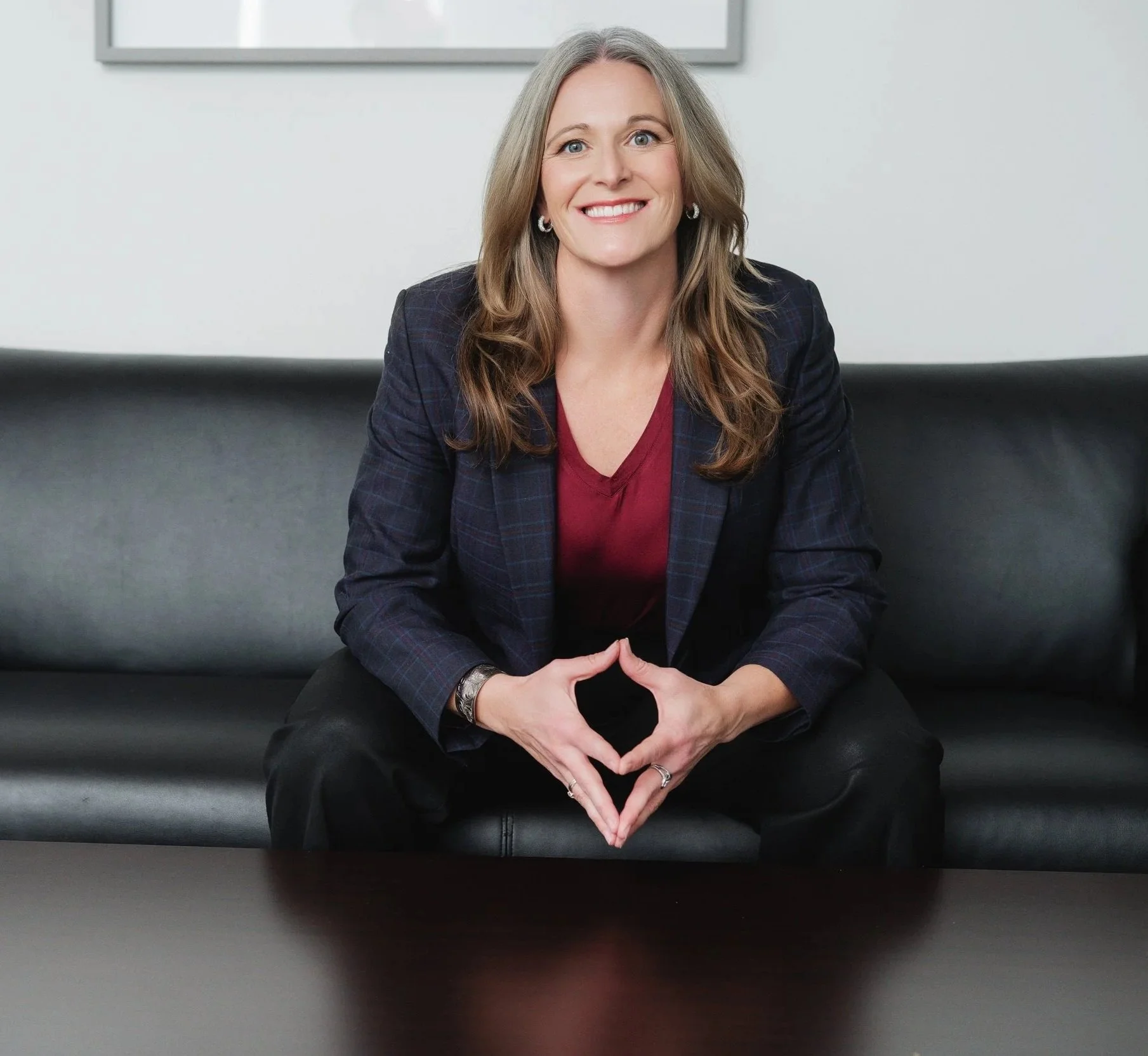 Separation and divorce coach Lana Wickstrom in Saskatoon sits on a black leather couch in a professional setting, smiling at the camera with her hands clasped in a heart shape.