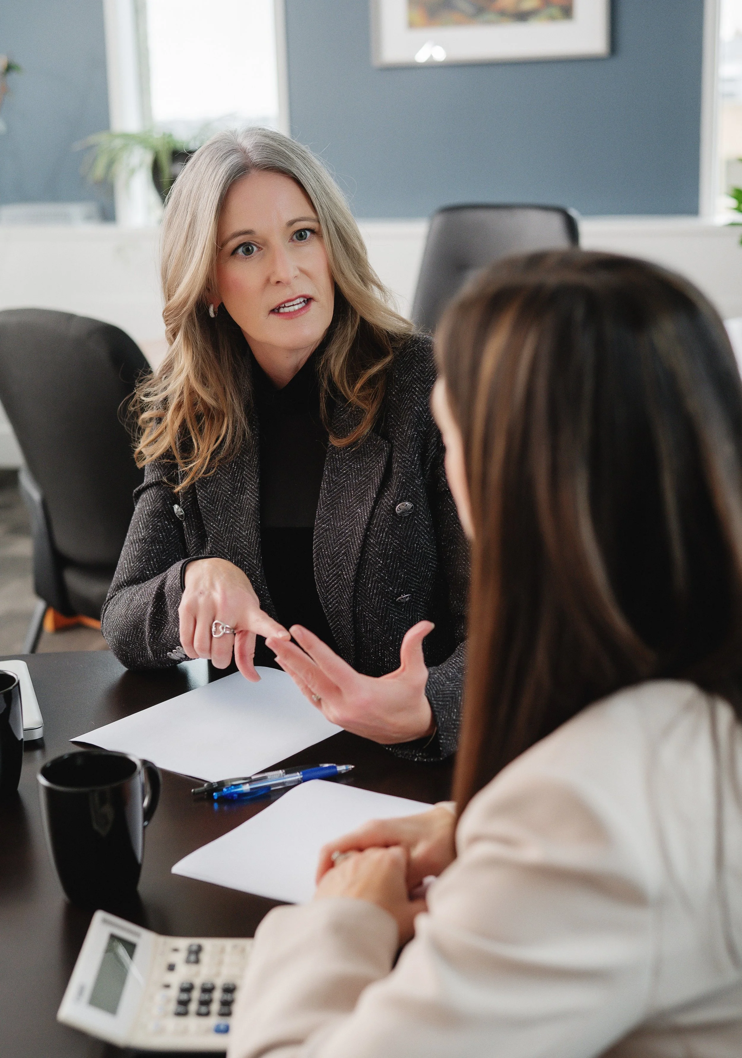 Separation and divorce coach Lana Wickstrom in Saskatoon is talking to another woman at a meeting table, gesturing with her hands, with papers and a calculator on the table.