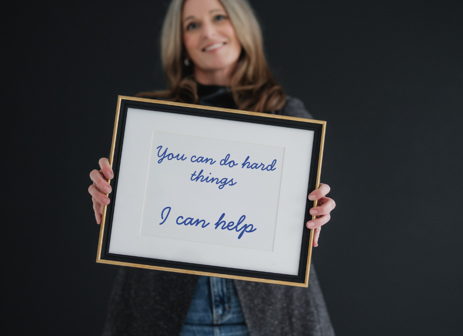 Separation and divorce coach Lana Wickstrom in Saskatoon is holding a framed sign with the message, "You can do hard things. I can help," against a dark background.